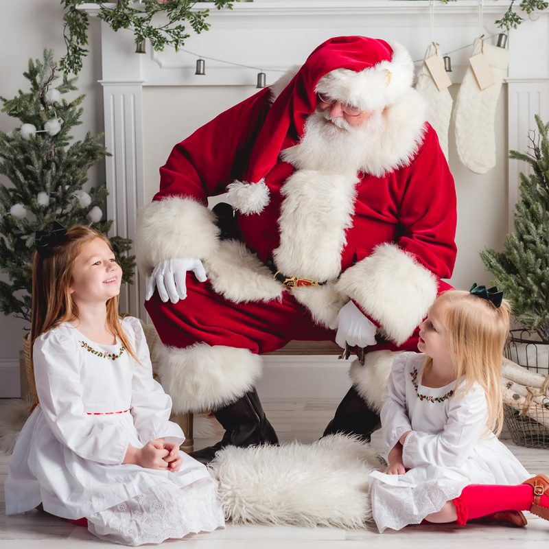 51_CT_SANTA_MINI_PHOTO_SESSIONS_KELLI_DEASE Two young girls dressed in holiday pajamas sitting at the feet of Santa during a Connecticut holiday mini session