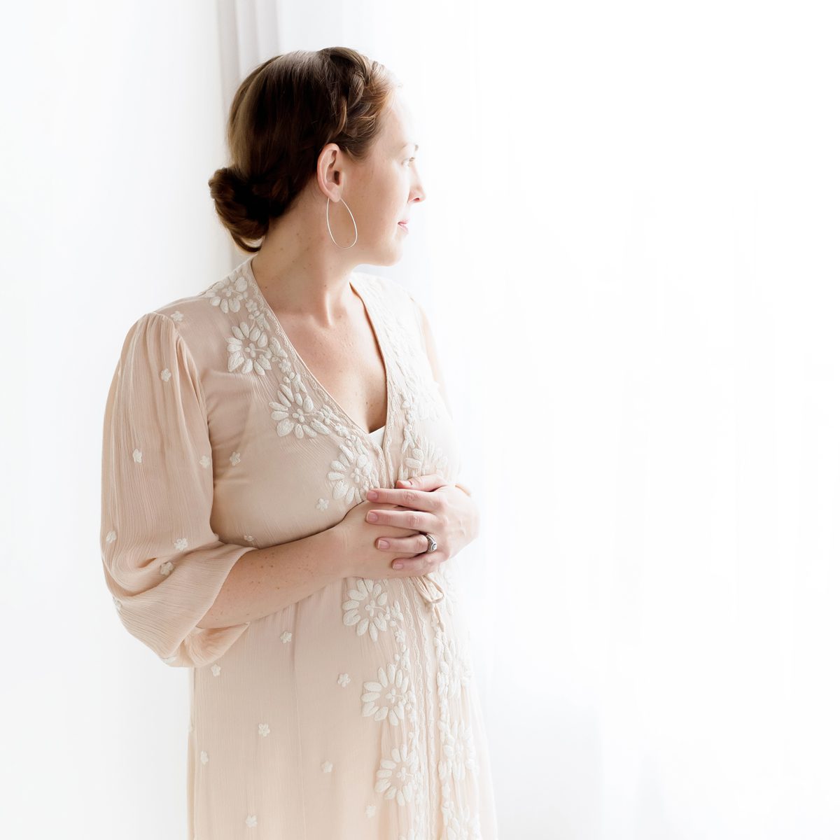 2024 Maternity Portfolio CT Photographer 1200px_09 A pregnant woman holding her belly and gazing out the window in a Connecticut maternity photo studio