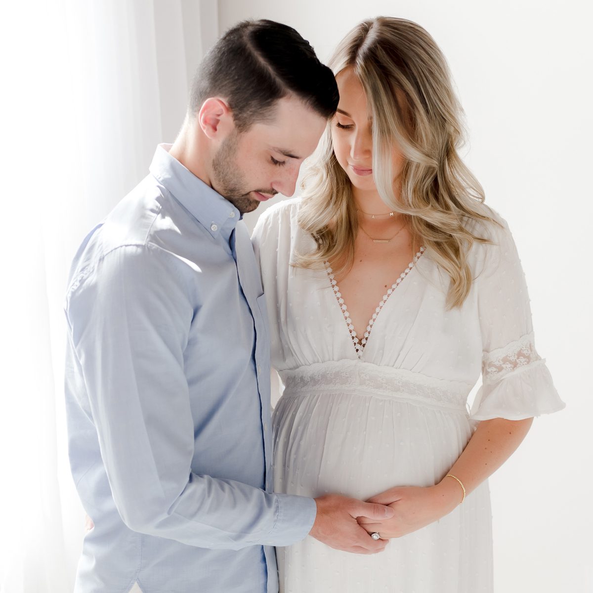 2024 Maternity Portfolio CT Photographer 1200px_12 A husband and wife embracing during a maternity photo session. They are holding hands and gently touching her pregnant belly.