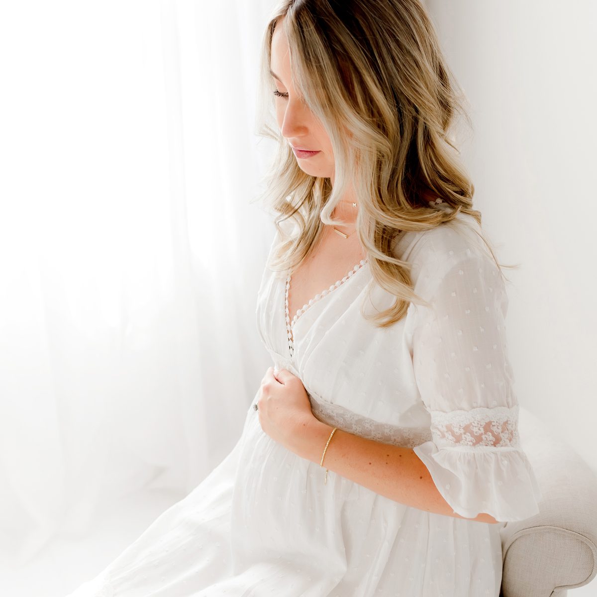 2024 Maternity Portfolio CT Photographer 1200px_14 An expectant mother wearing a white, flowy dress, cradling her belly in Connecticut photography studio in a light and airy style.