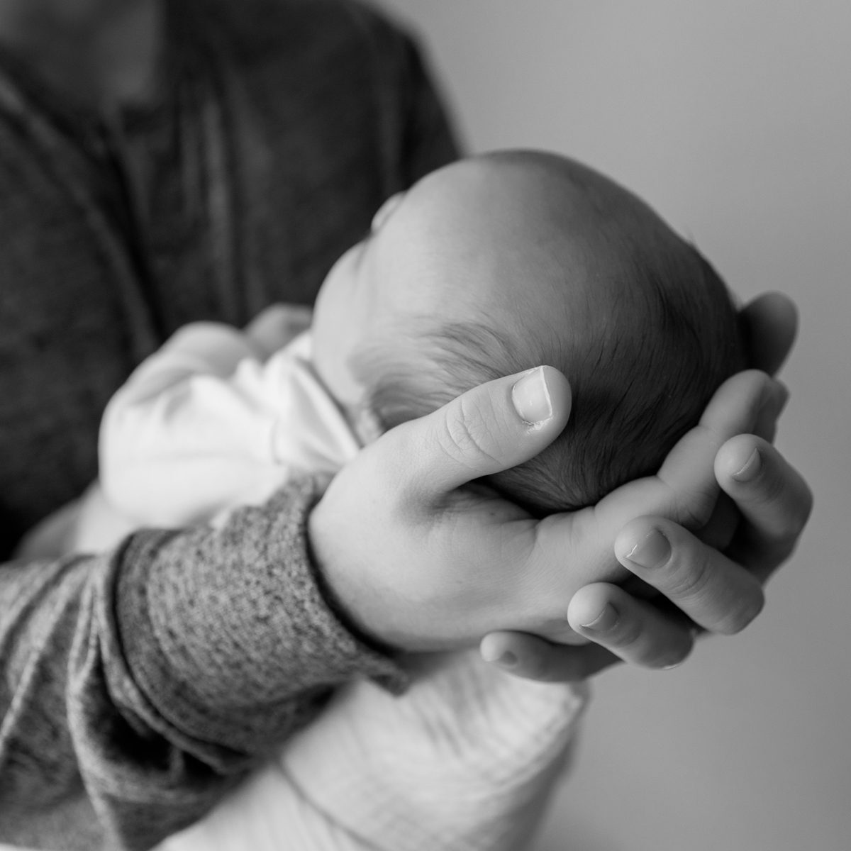 Black and white close-up studio portrait of a sleeping newborn baby cradled in a parent's hands, photographed in a quiet minimalist style by a Connecticut newborn photographer.