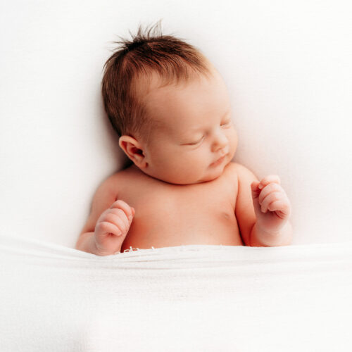 Natural newborn photography on a white backdrop, light and airy style. A gentle, peaceful setting with a baby in natural poses, highlighting their innocence and purity. The environment should feel serene and warm, perfect for families in Farmington, Canton, Avon, West Hartford, and Simsbury, Connecticut.