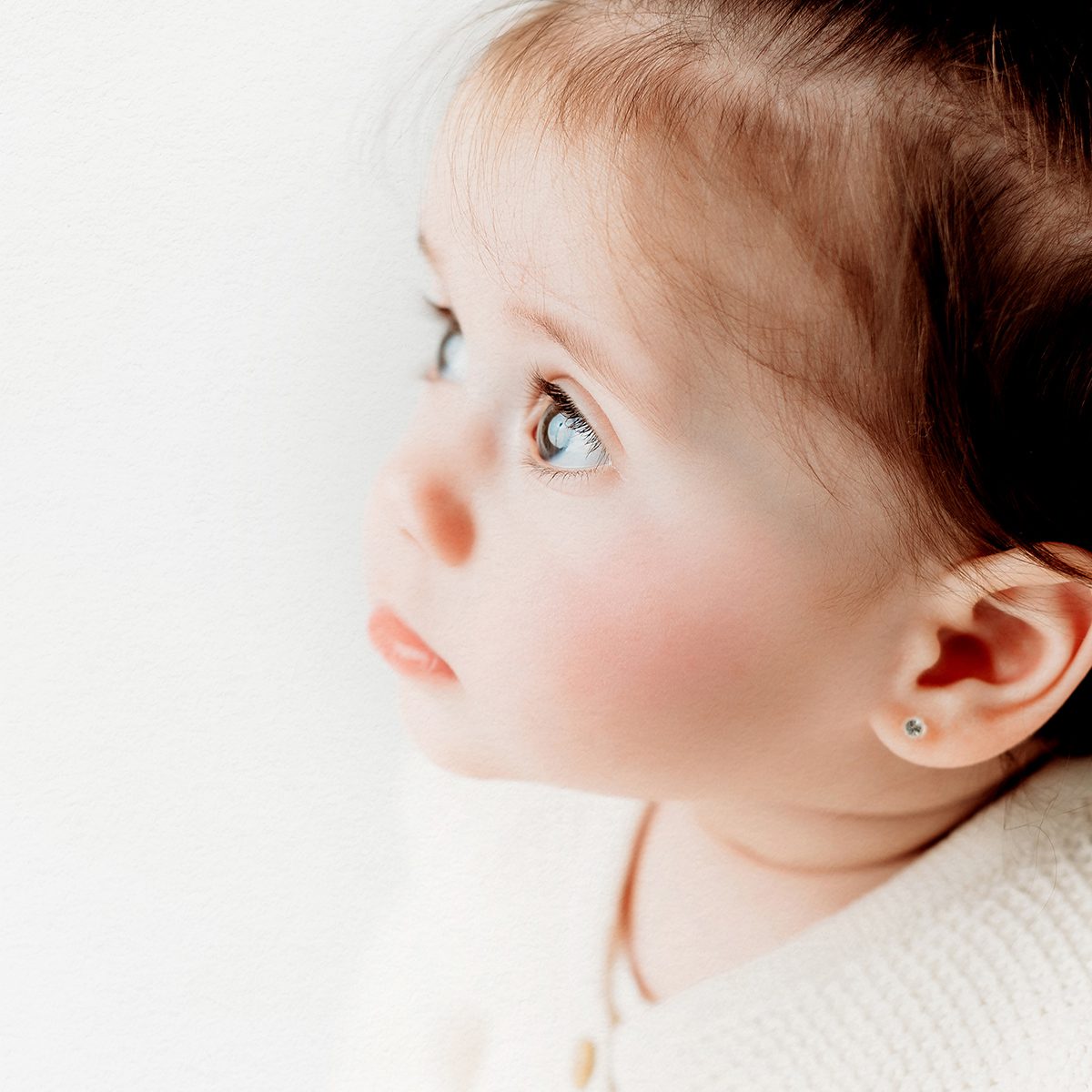 Close-up profile of baby girl with bright blue eyes and soft natural light, photographed against a white background during a Connecticut baby photography session.