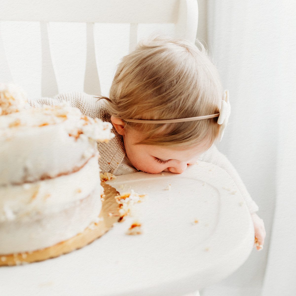 One-year-old baby girl leaning over a white cake during a first birthday cake smash session in a bright Connecticut studio.