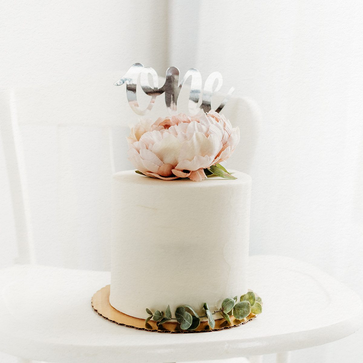 2025 Portfolio CT Birthday Photographer 1200px_10 Minimalist first birthday cake with white frosting, blush peony topper, and “one” cake topper, styled on a white backdrop for a Connecticut cake smash session.