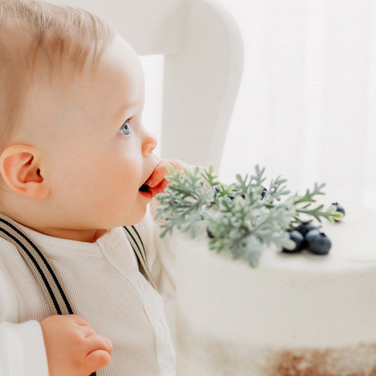 2025 Portfolio CT Birthday Photographer 1200px_11 Baby boy in a cream romper with suspenders sitting in a white high chair during a first birthday session at Kelli Dease Photography in Farmington, CT