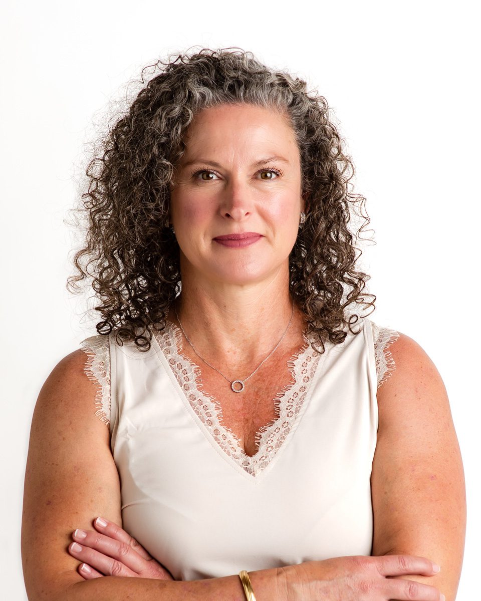 a casual headshot of an older woman with gray curly hair wearing a sleeveless silk blouse