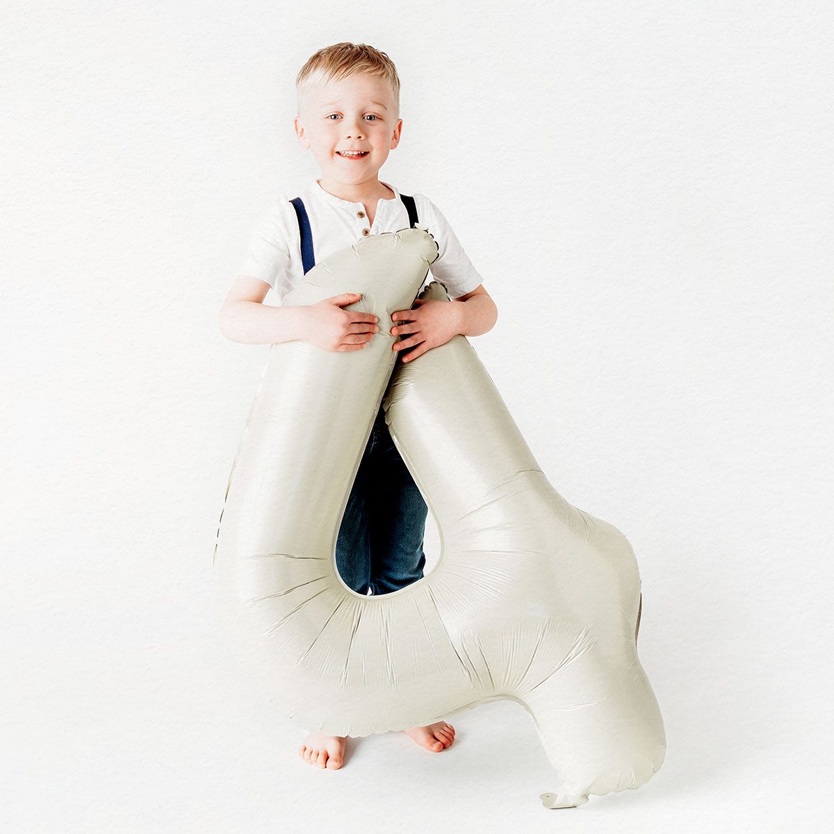 A blonde little boy holding a number four birthday balloon. He is smiling at the camera during his Farmington, CT, birthday photo shoot.