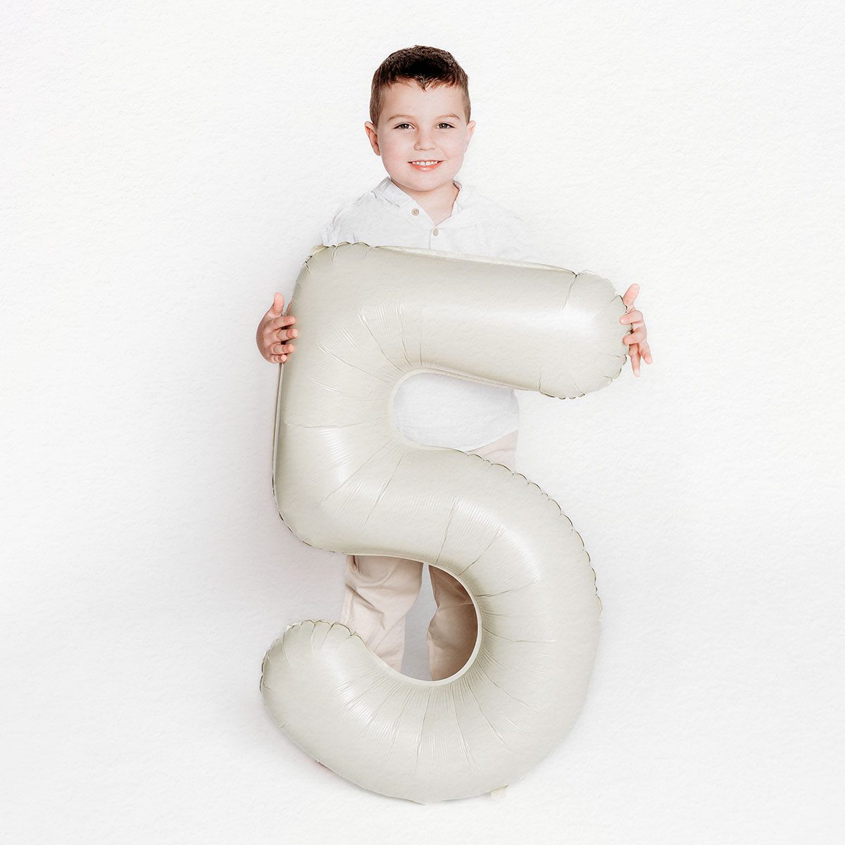 2025 Portfolio CT Birthday Photographer 1200px_18 A five-year-old little boy holding a number five birthday balloon, photographed in a white indoor studio in Farmington, CT