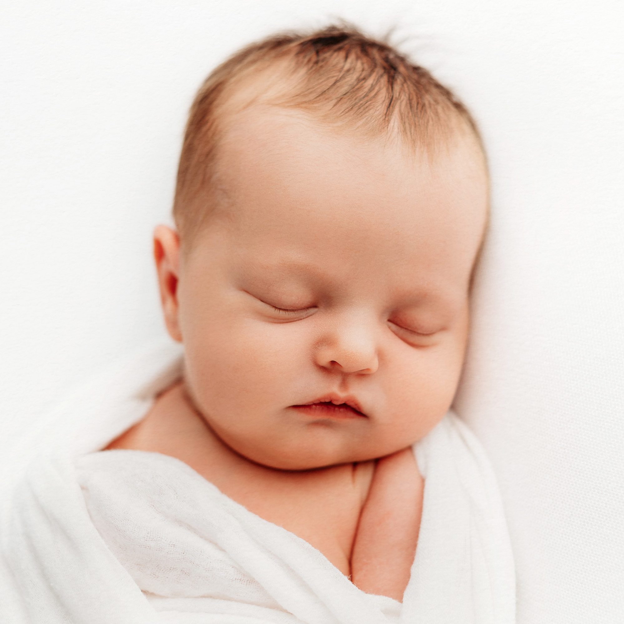 Natural baby photography on a white backdrop, light and airy style. A gentle, peaceful setting with a baby in natural poses, highlighting their innocence and purity. The environment should feel serene and warm, perfect for families in Farmington, Canton, Avon, West Hartford, and Simsbury, Connecticut.