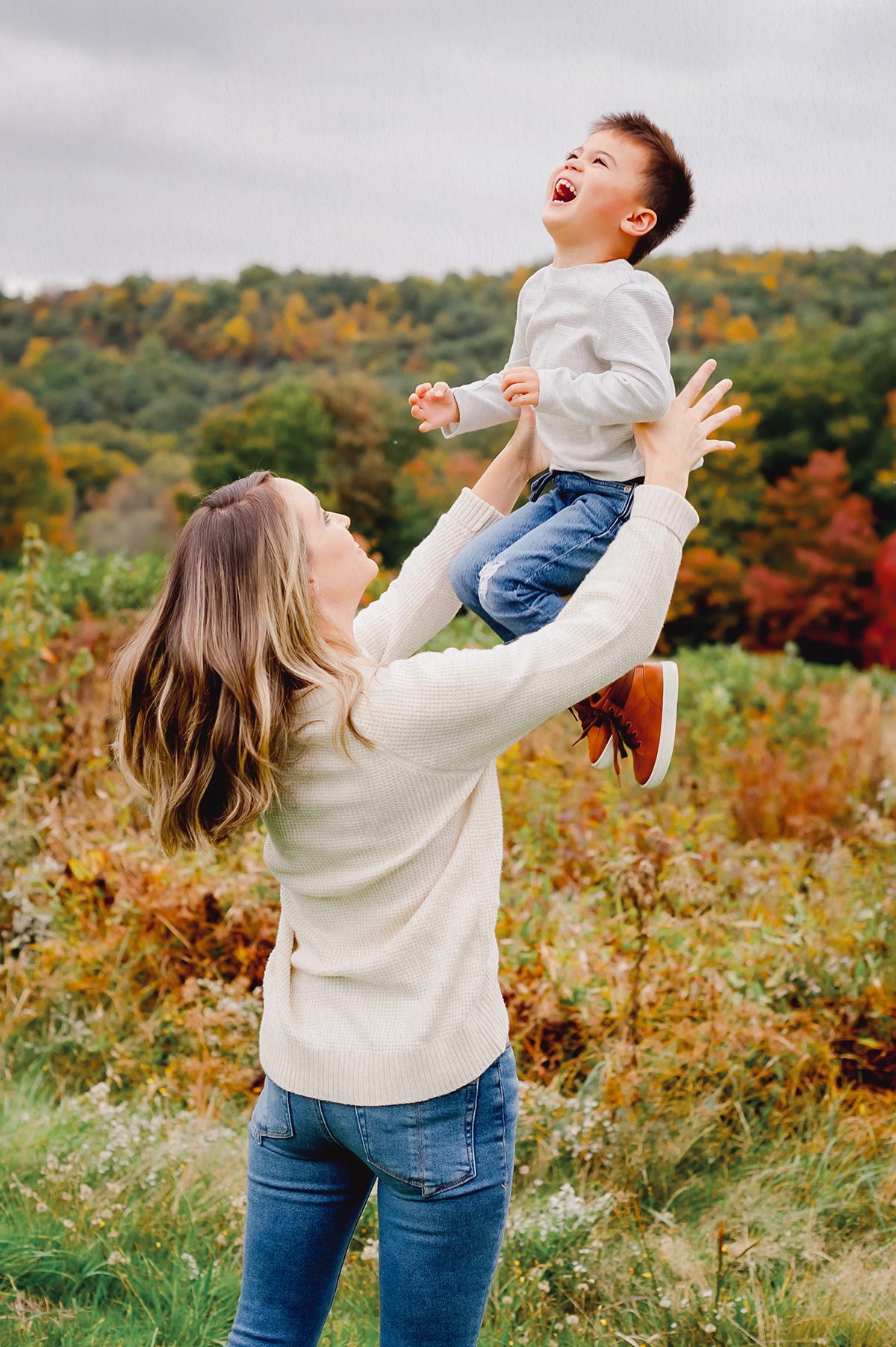 Fall family photoshoot in Simsbury CT featuring a mother tossing her son in the air in a colorful autumn field.