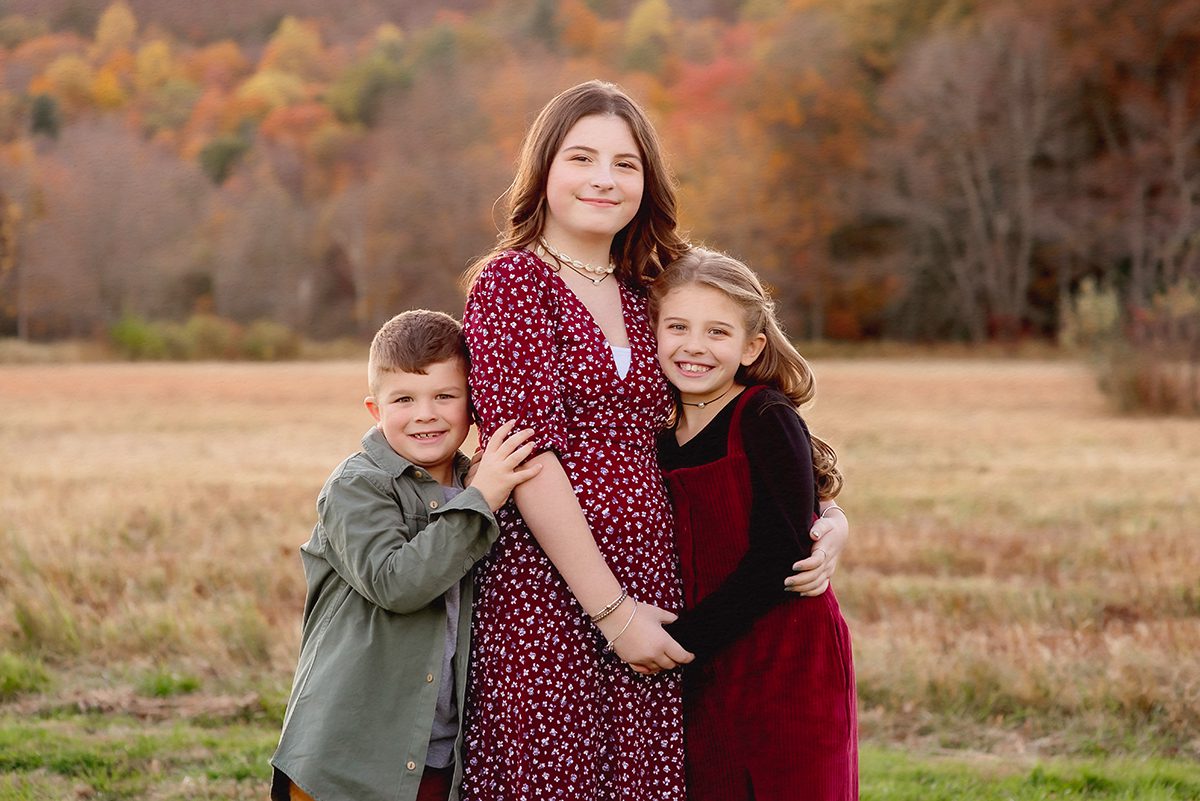 Fall family photoshoot in Farmington CT featuring three children in coordinating burgundy outfits in a colorful autumn field.