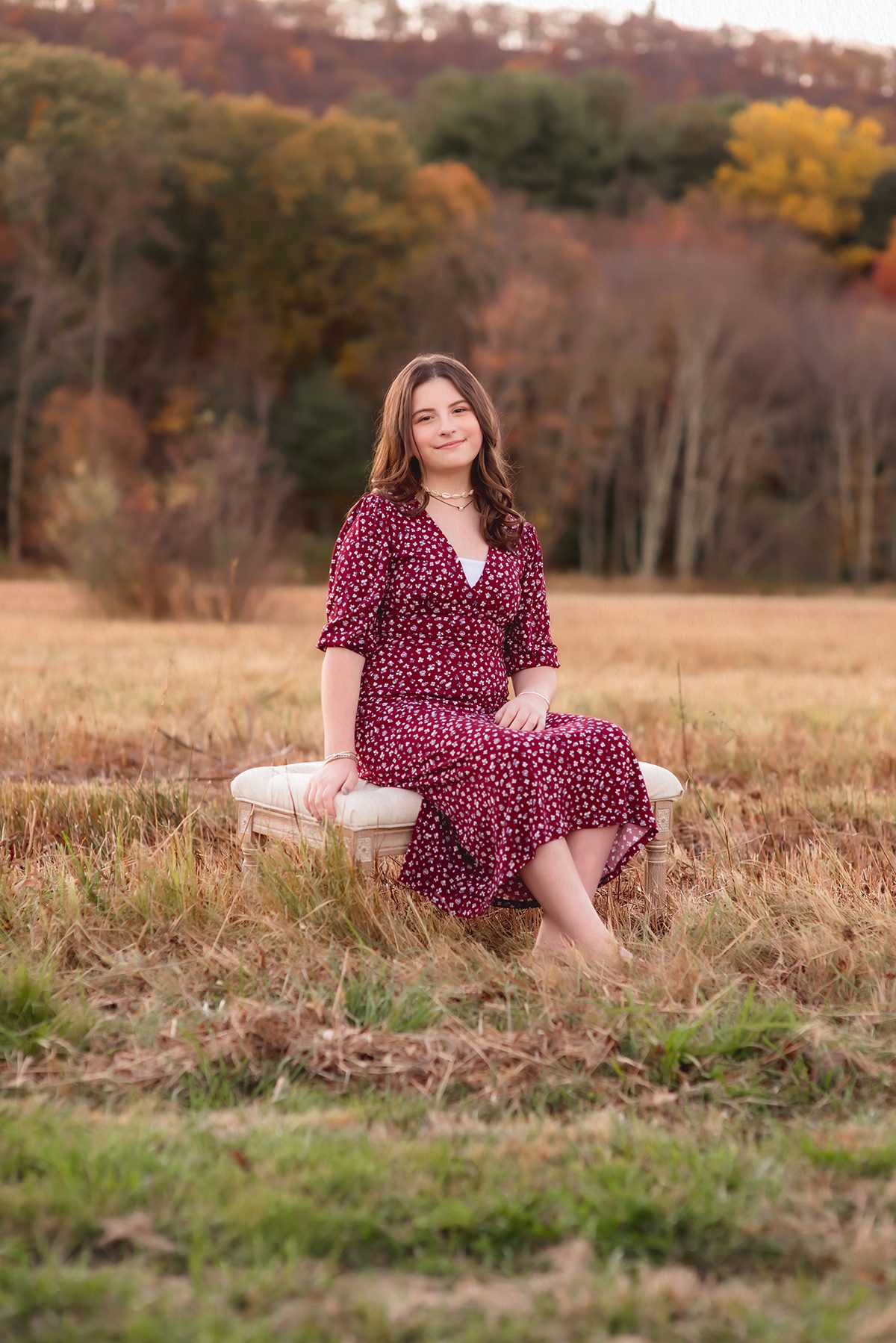 A tween girl sitting on a bench in an open field in fall, surrounded by autumn colors and soft golden hour light.