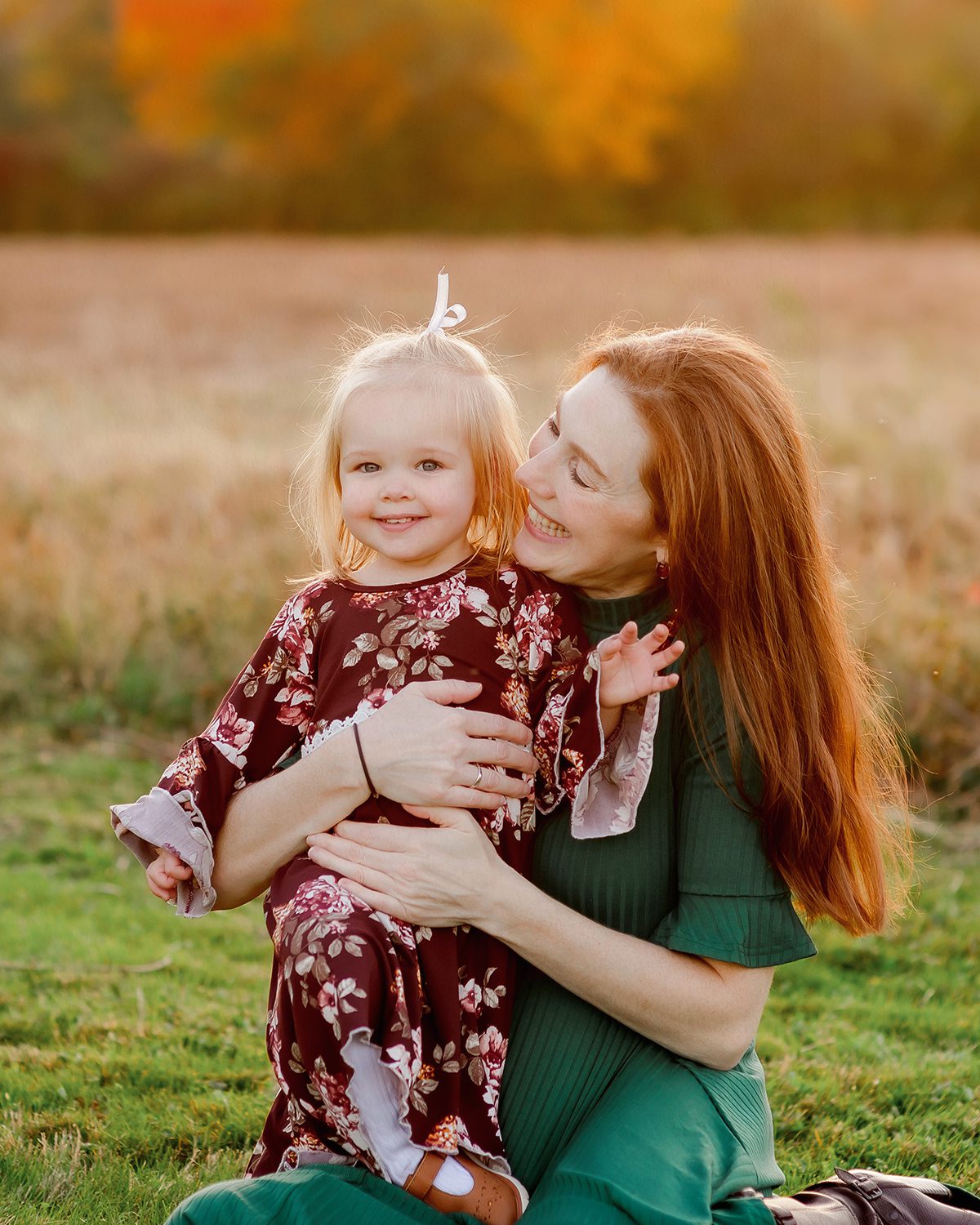 A mom and daughter in an open field in fall, surrounded by autumn colors and soft golden hour light.