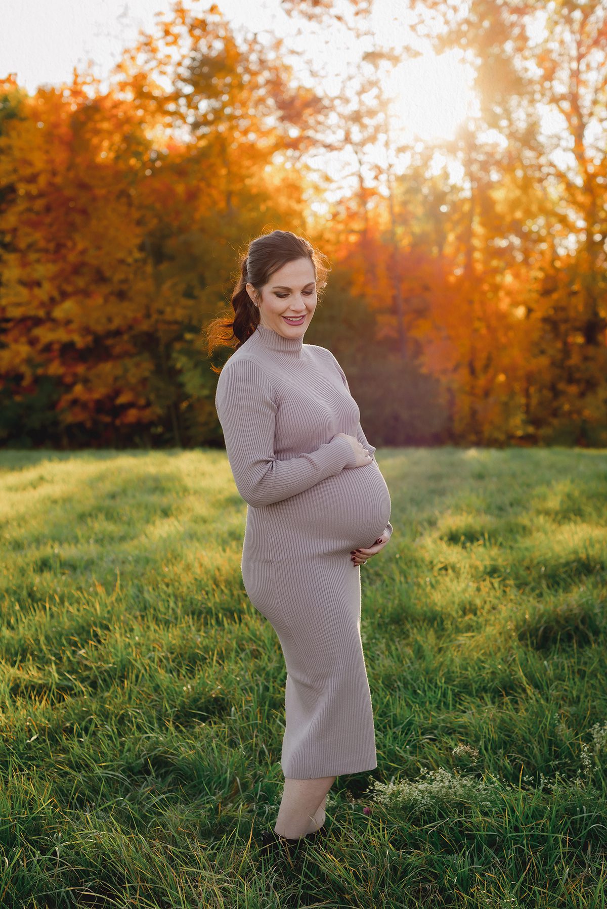 Fall maternity photos in CT field at golden hour – expecting mom in fitted taupe dress with autumn backdrop.
