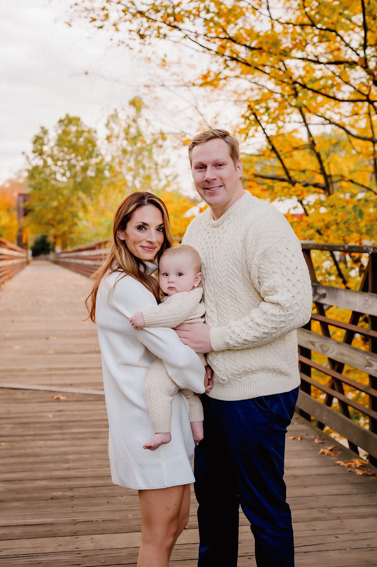 Fall family photo on covered bridge near Canton CT with golden leaves and cozy ivory sweaters. Best time for outdoor family photos in fall – cozy neutral outfits and natural golden light in Connecticut.