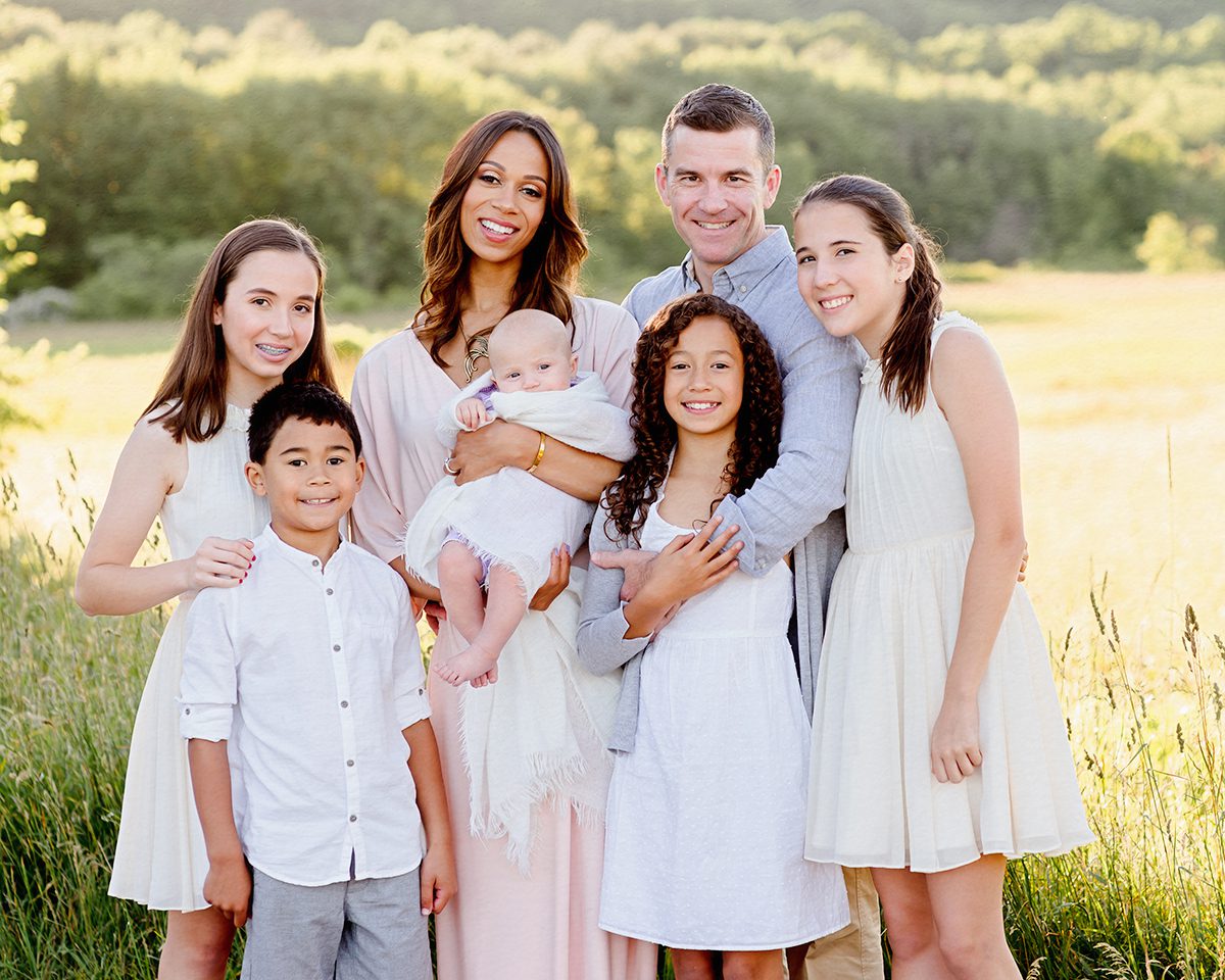 Sunset family photo session in a golden field featuring a blended family with an older newborn and five siblings, showcasing natural connection and relaxed outdoor styling.