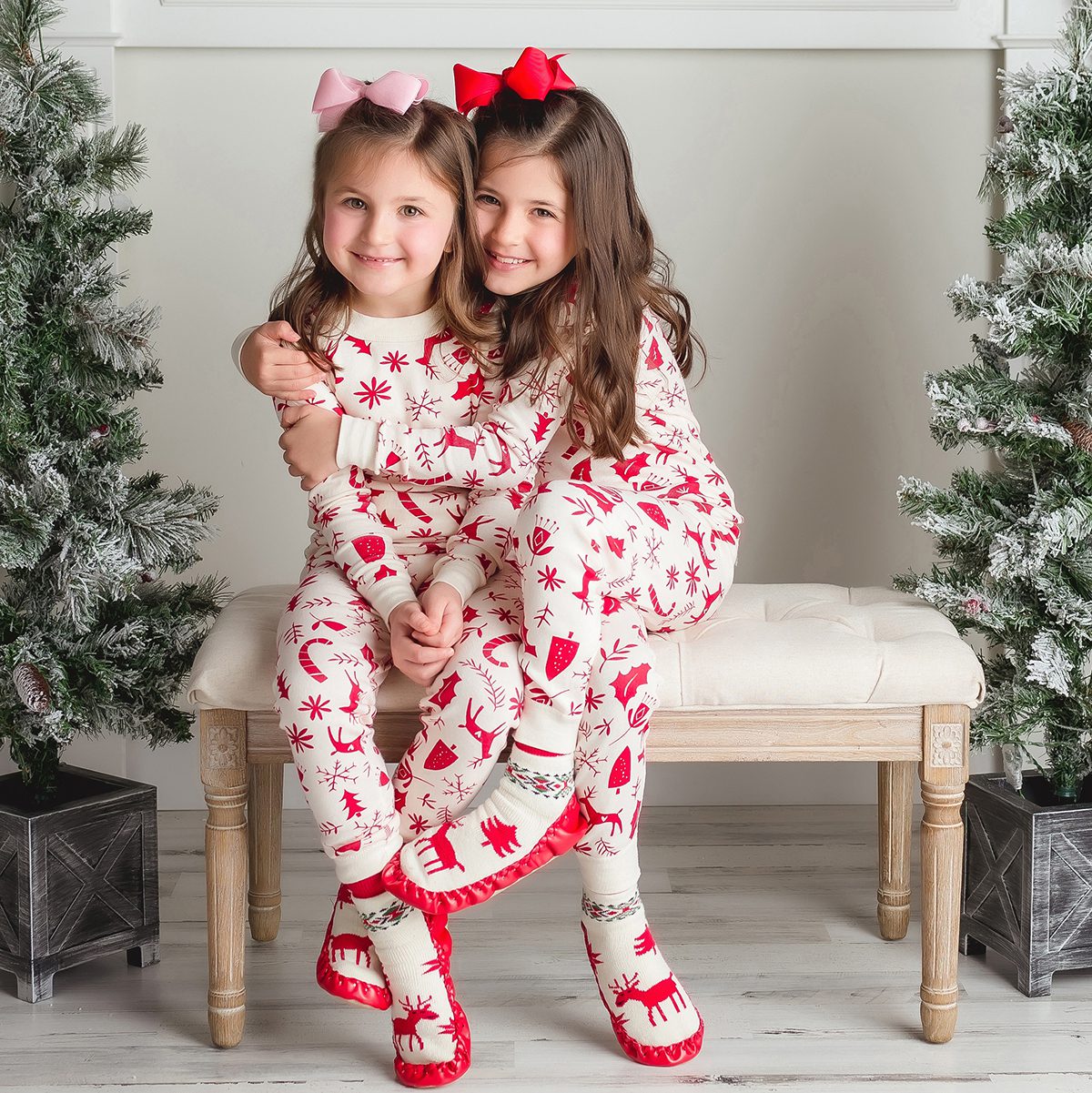 Two siblings laughing together while sitting on a bench decorated with holiday garland.