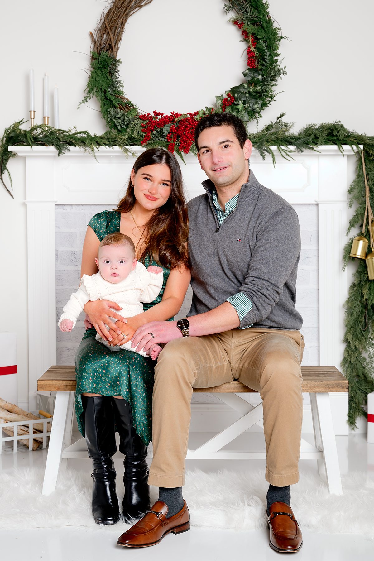 Family of three sitting on a bench decorated with holiday garland.