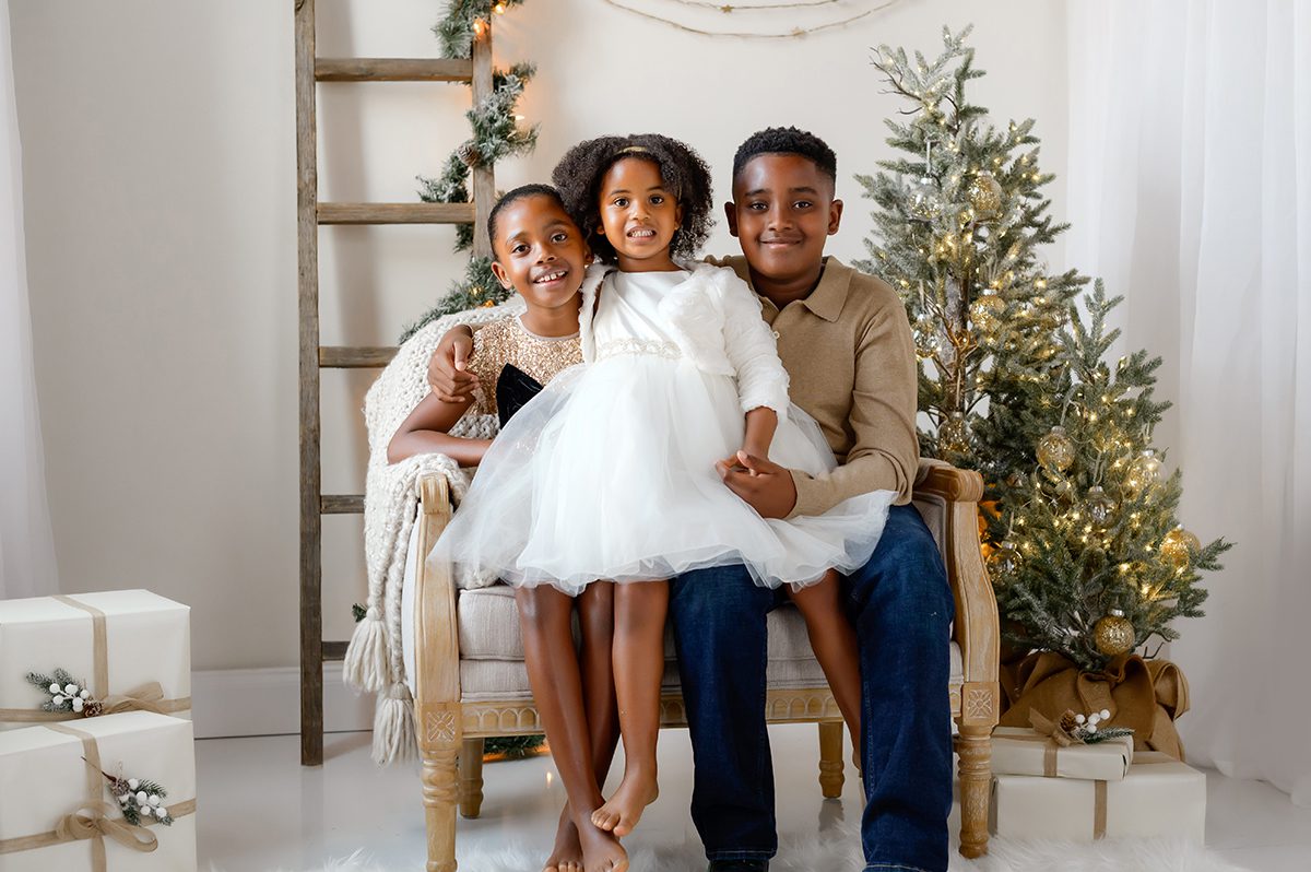 Three siblings sitting on a chair during a christmas photo shoot.