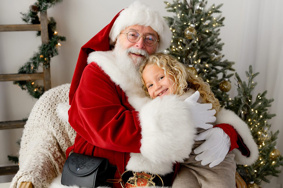 Child hugging santa, smiling while chatting during a studio Santa session.