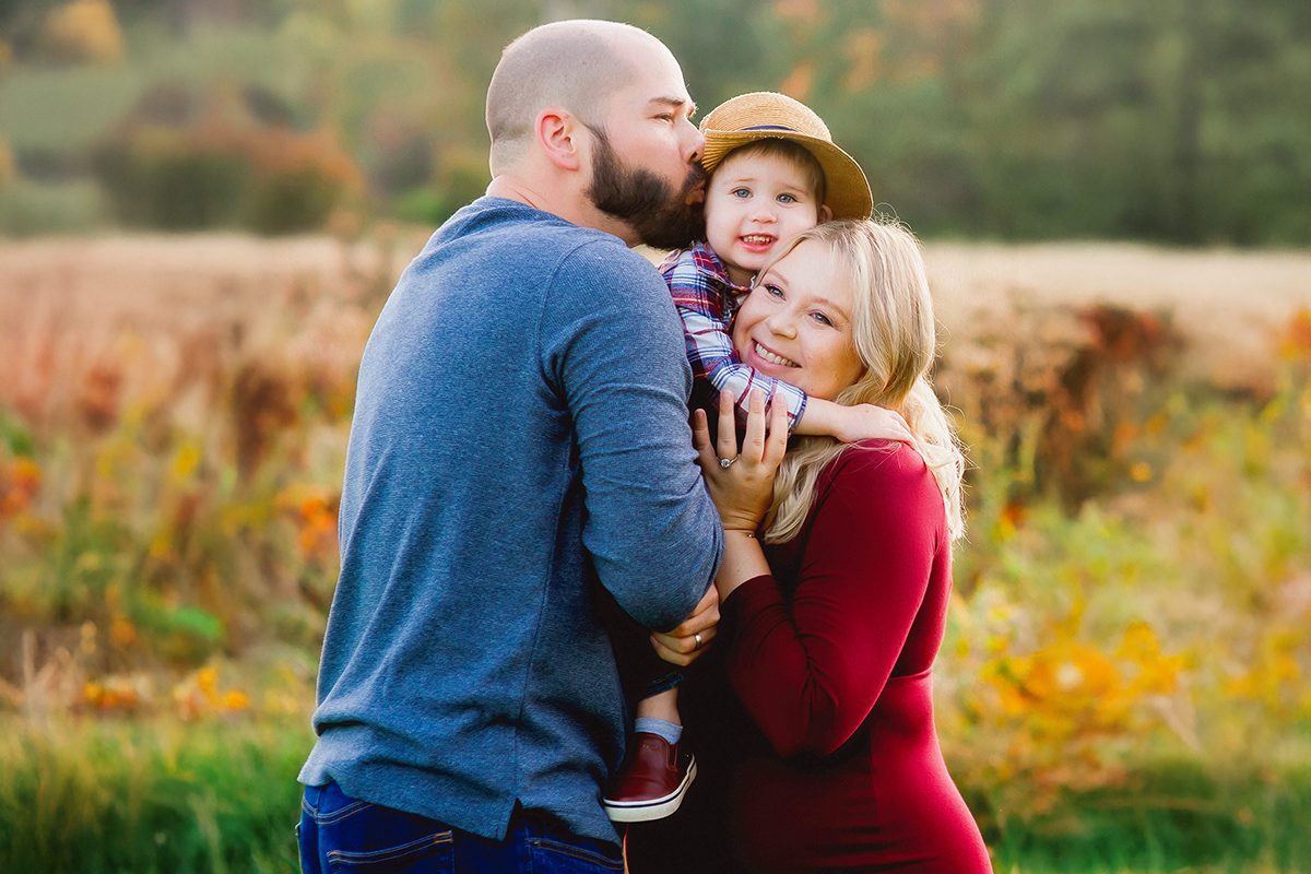 Fall family pictures with toddler in Connecticut – playful outfit ideas and natural, candid moments. Candid fall family photography in Connecticut field with warm, earthy wardrobe for parents and child.