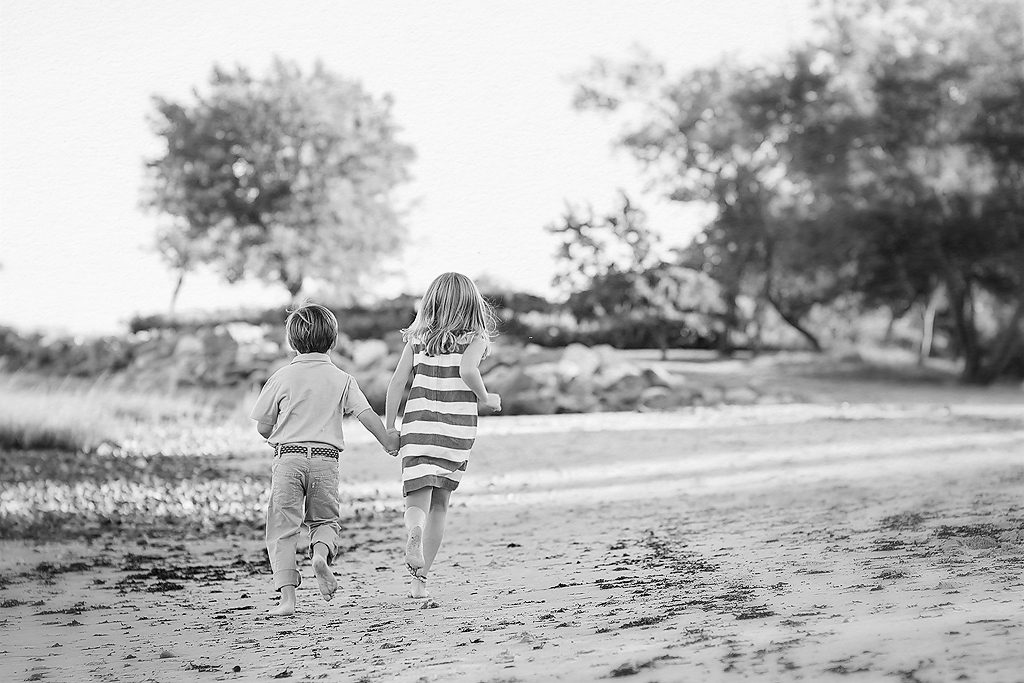black and white photo of a brother and sister running on the beach by connecticut family photographer kelli dease