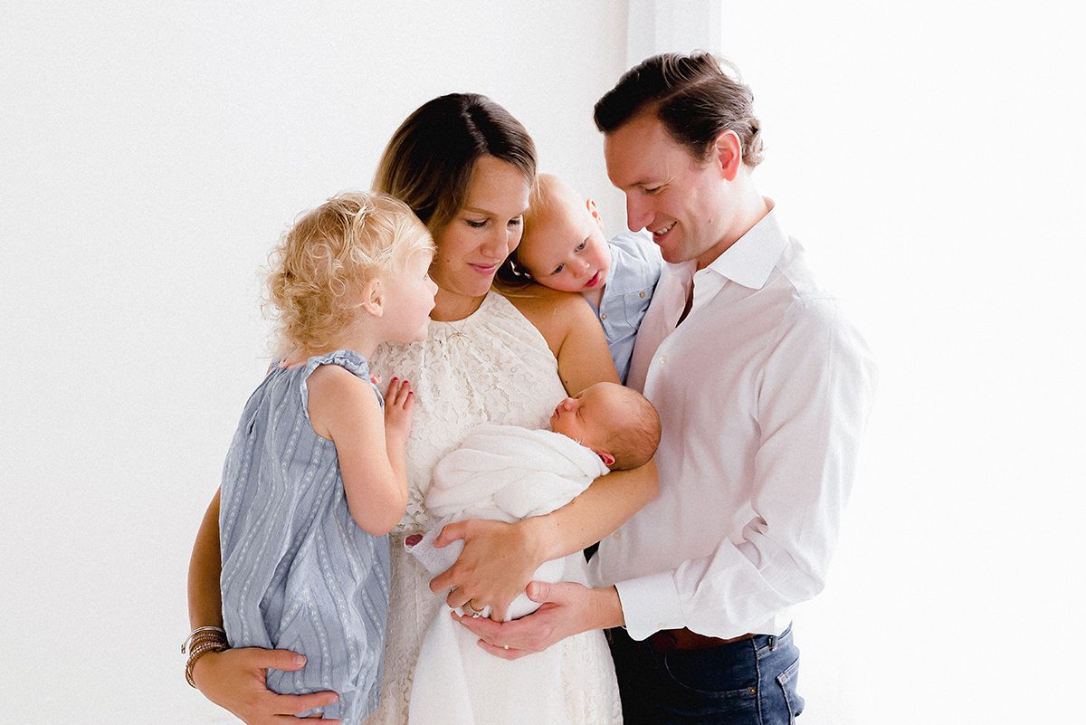 Studio newborn family portrait with parents and young siblings gathered around their newborn baby, photographed by a Farmington, Connecticut newborn photographer.