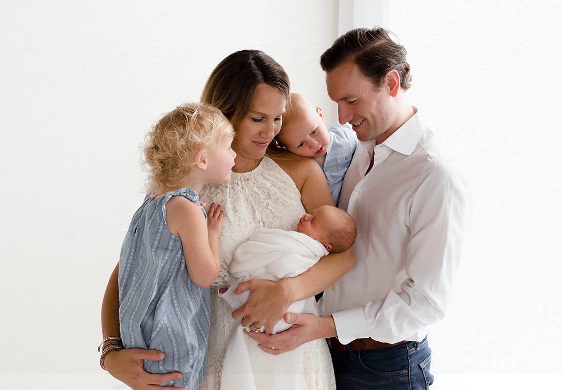 Studio newborn family portrait with parents and young siblings gathered around their newborn baby, photographed by a Farmington, Connecticut newborn photographer.