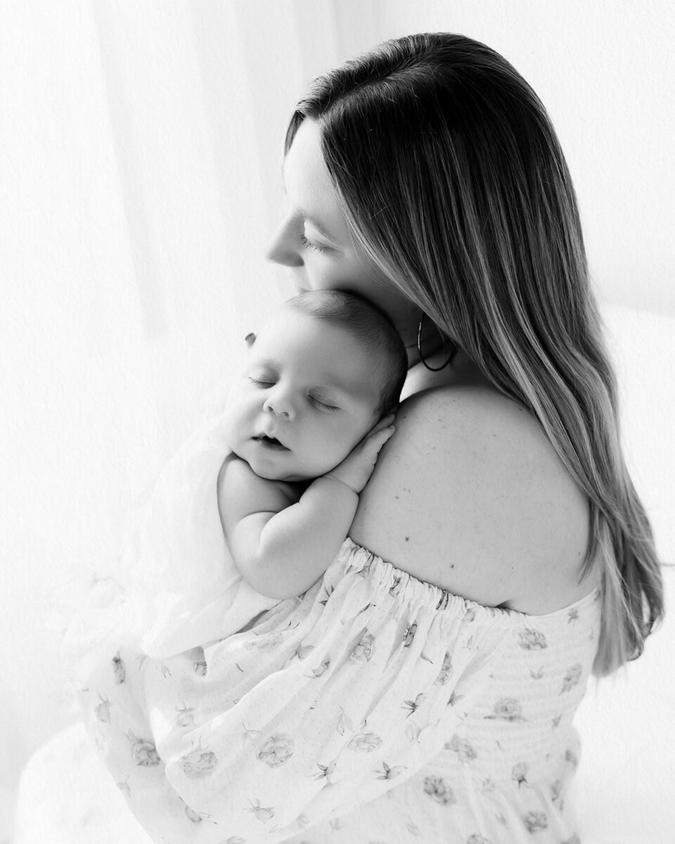 Black and white lifestyle newborn portrait of a mother holding her sleeping baby against her shoulder, captured in natural light during a Connecticut newborn photography session.