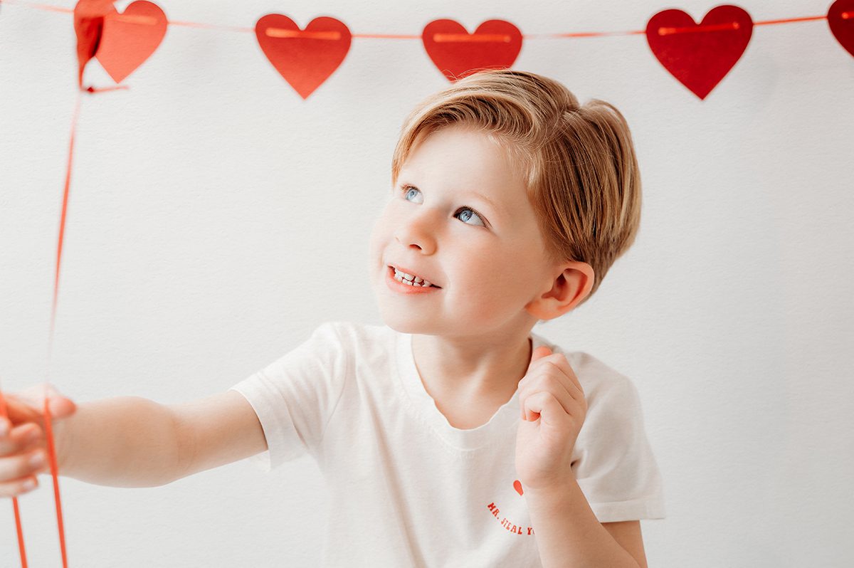 Valentine’s Day studio portrait of a 4 year old boy holding red heart balloons