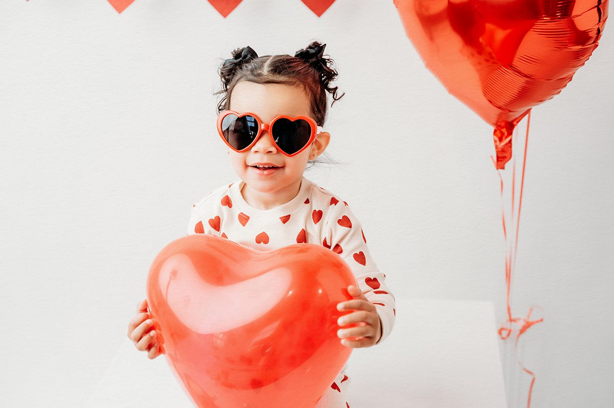 Toddler Valentine mini session portrait with red heart balloons and simple, timeless styling