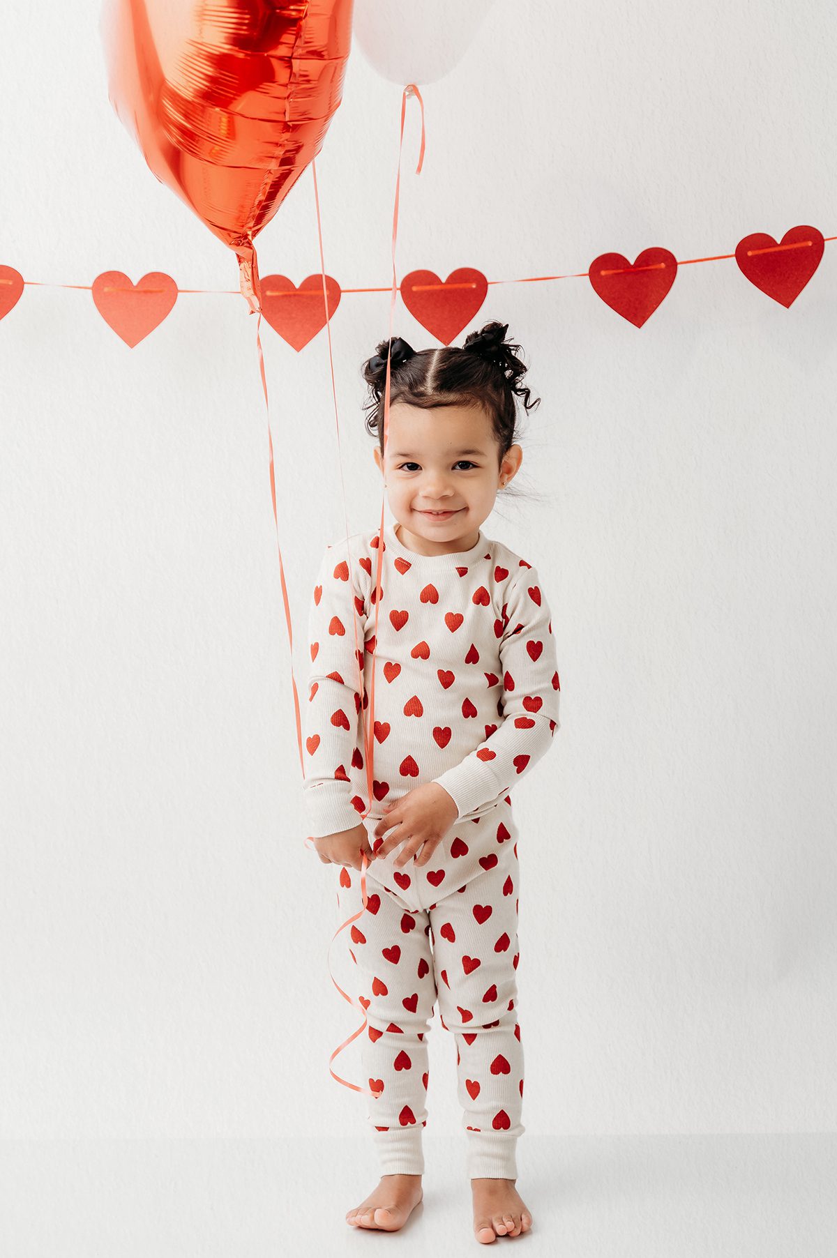 Playful child Valentine portrait with red heart decorations in a clean photography studio
