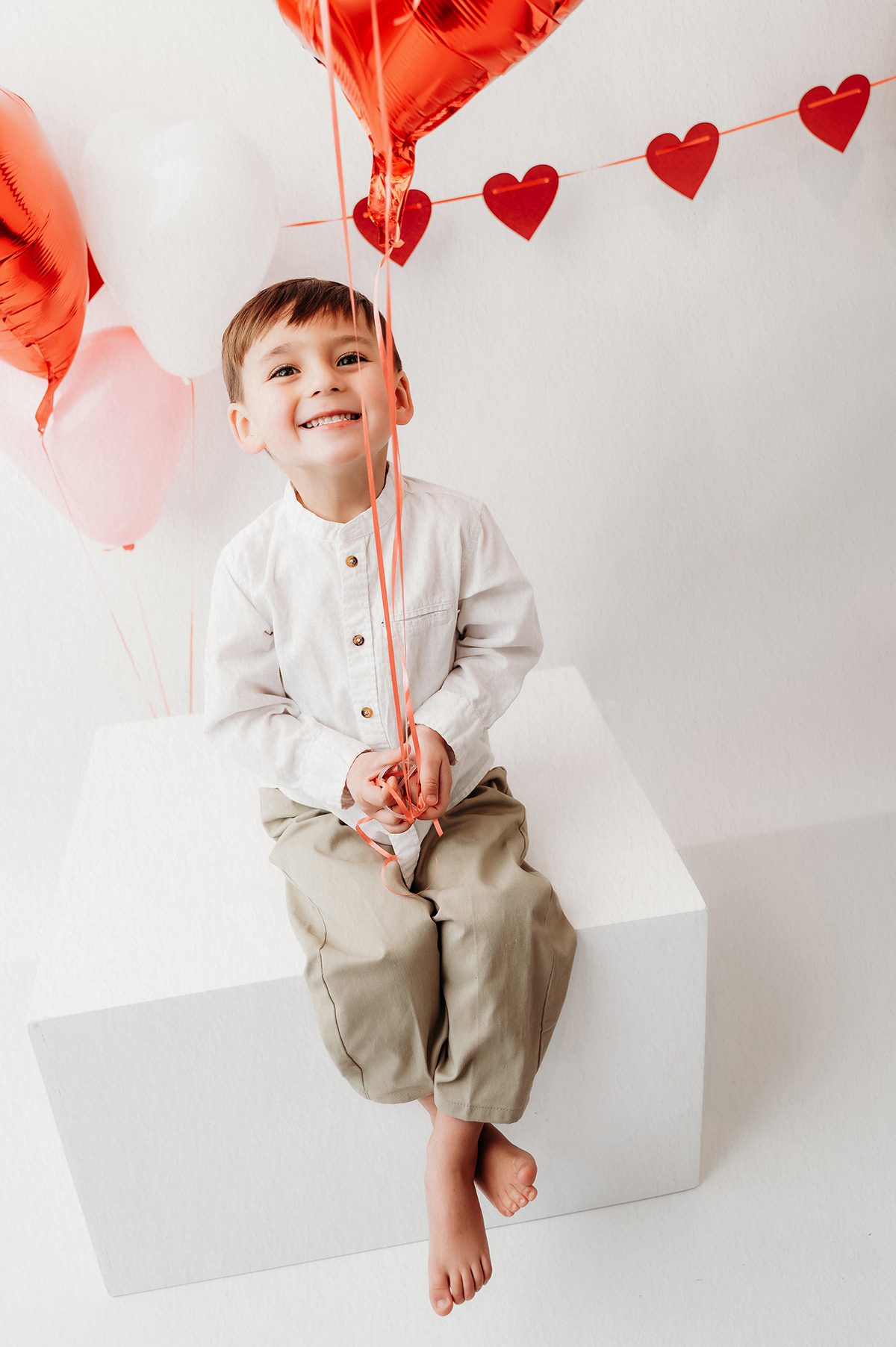 Sweet Valentine mini session portrait of a little boy sitting among red heart balloons