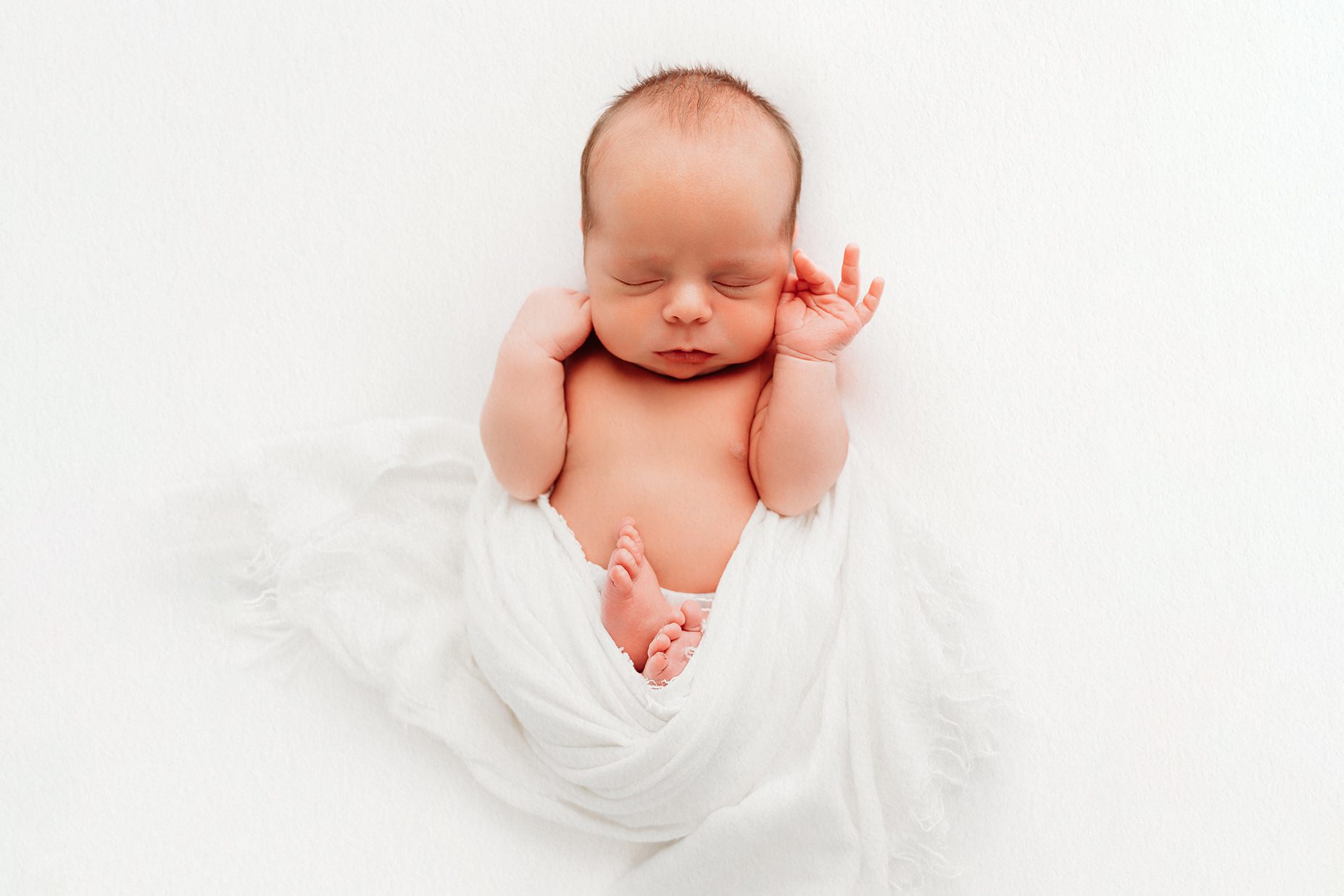 Sleeping newborn baby posed on a white backdrop with hands near face, photographed in a natural studio newborn session in Farmington, Connecticut.