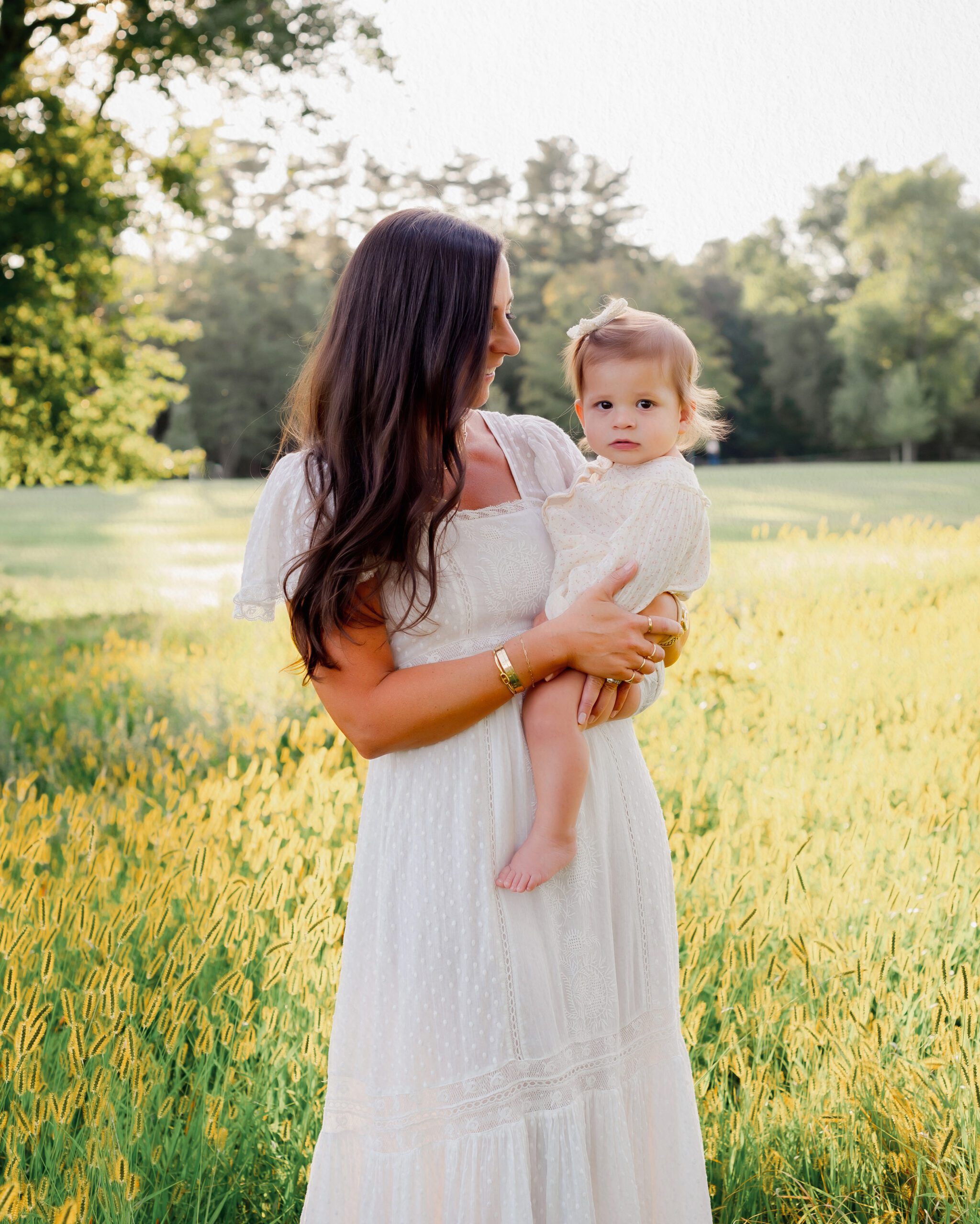 Mother holding her baby girl in a sunlit field during golden hour, captured during an outdoor family photography session in Connecticut.
