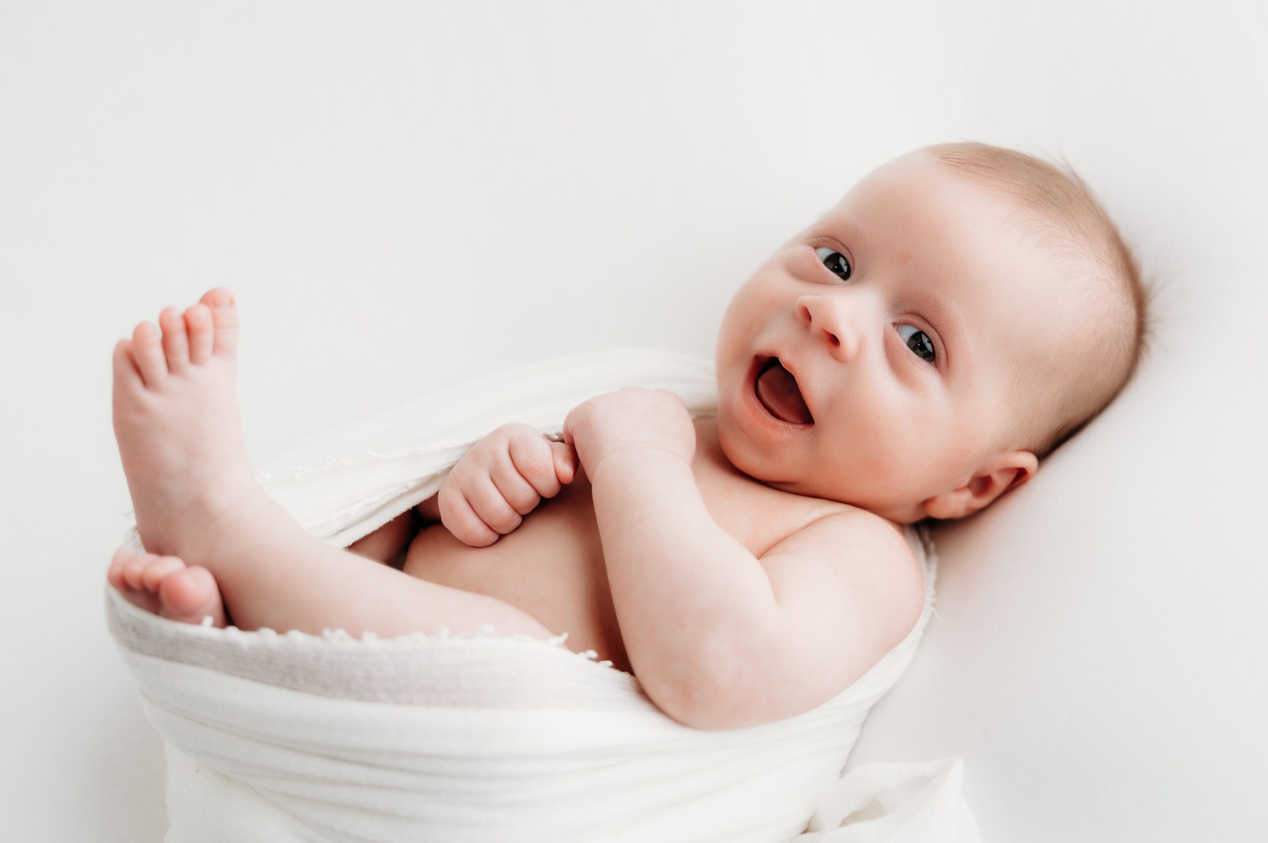 Smiling baby wrapped in a white blanket during a studio newborn session with Connecticut newborn photographer Kelli Dease