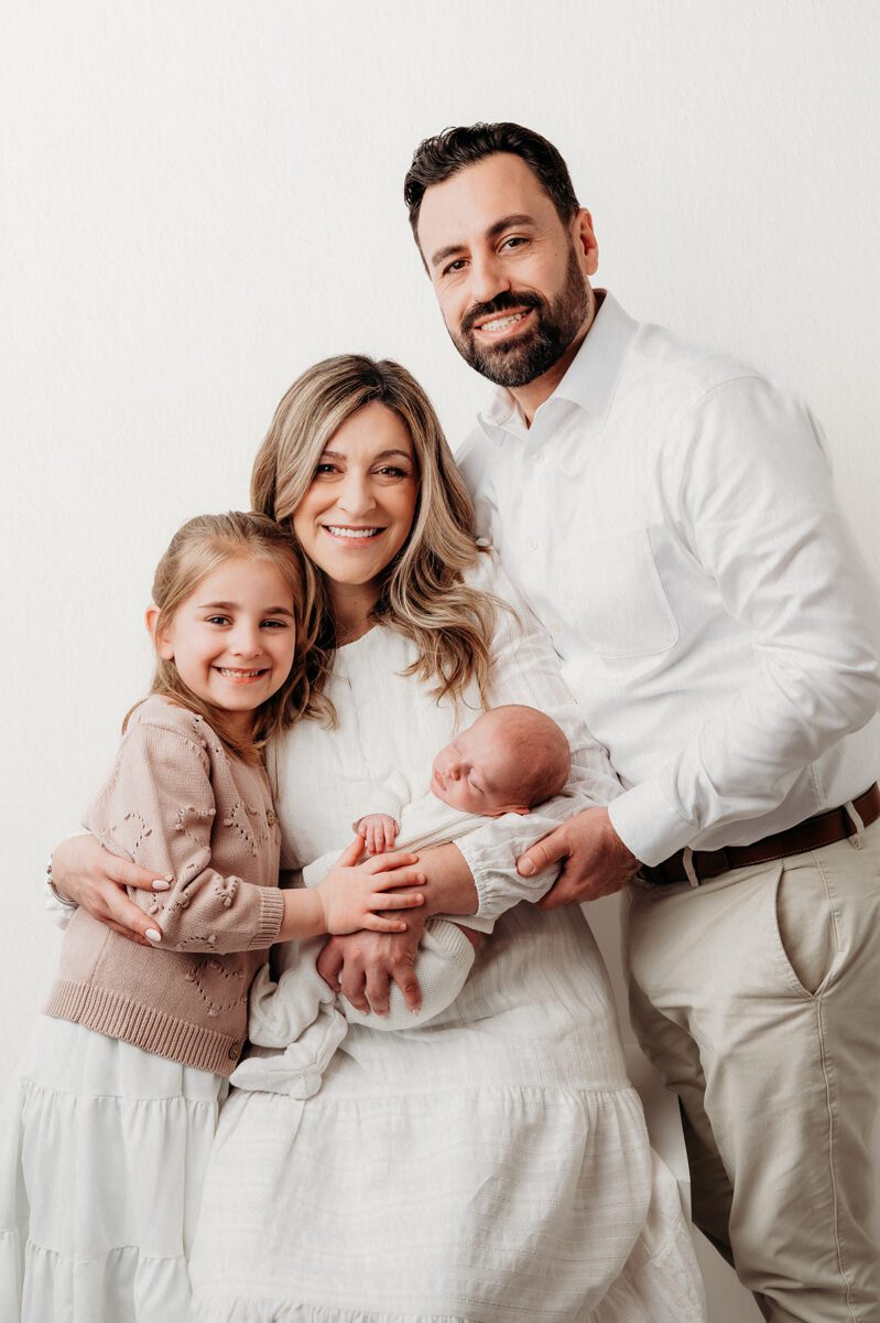 Parents and an older sibling wear soft neutrals and textures while holding a newborn during a studio family photoshoot, creating a timeless and cohesive look.