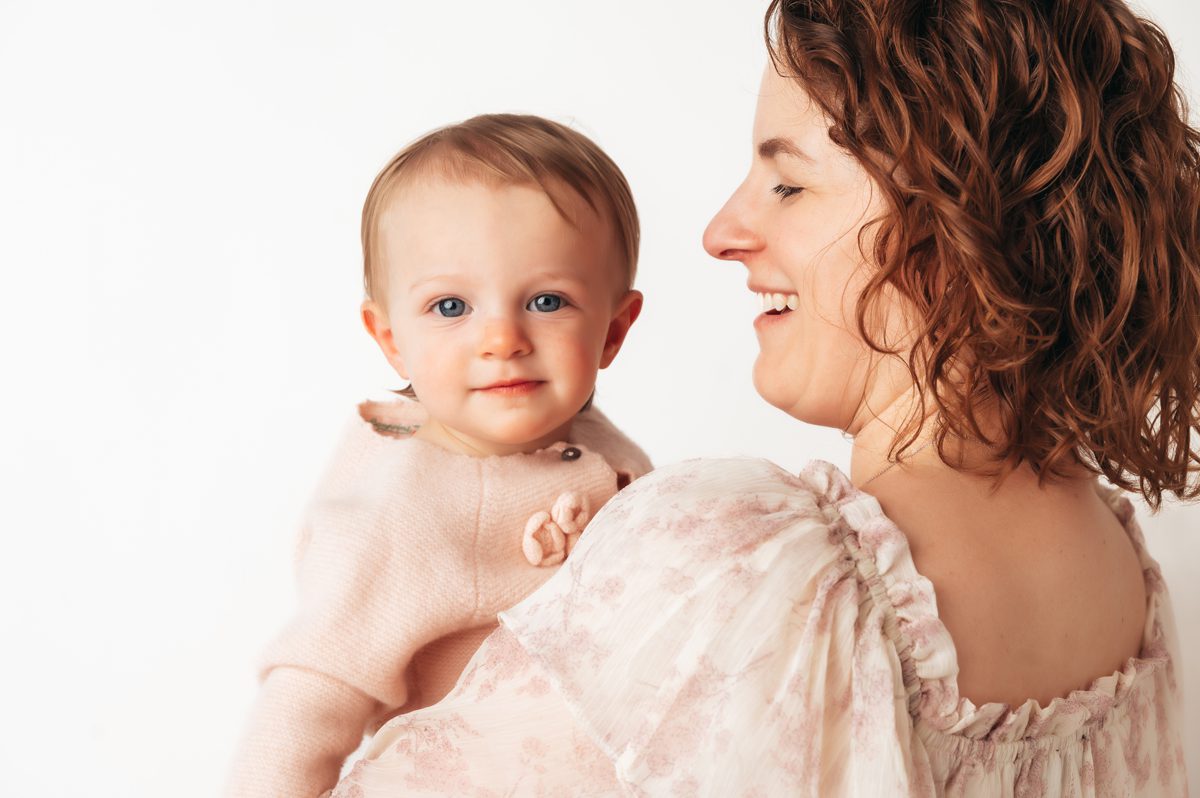 Close-up portrait of baby with blue eyes being held by smiling mom during a Connecticut motherhood mini session