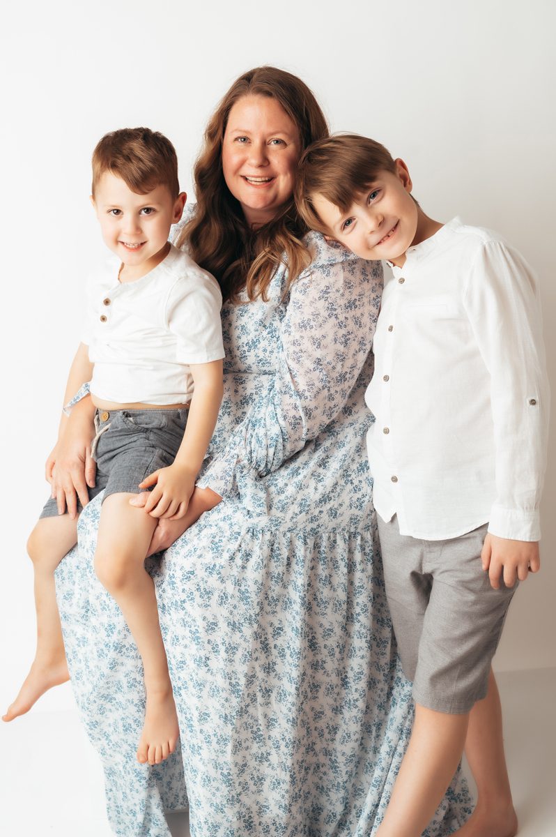 Mom smiling warmly with two sons leaning against her during a relaxed Connecticut motherhood mini session