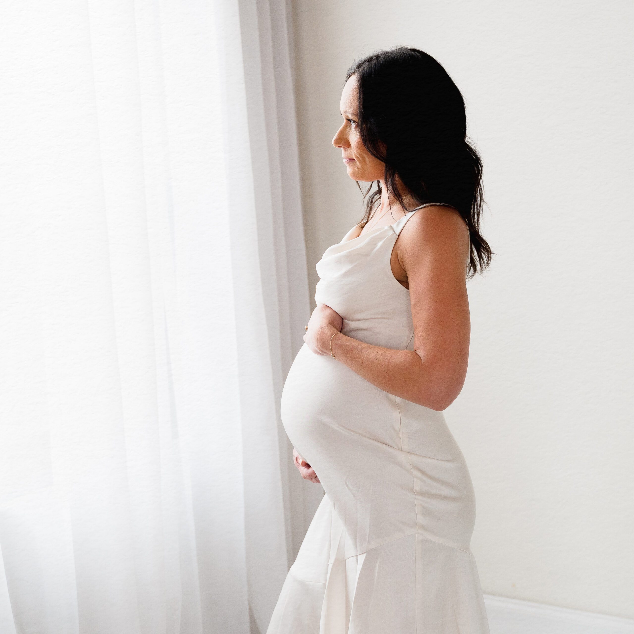 Pregnant woman in fitted cream dress dress in a solo studio maternity portrait taken in soft natural light by Kelli Dease Photography in Farmington CT