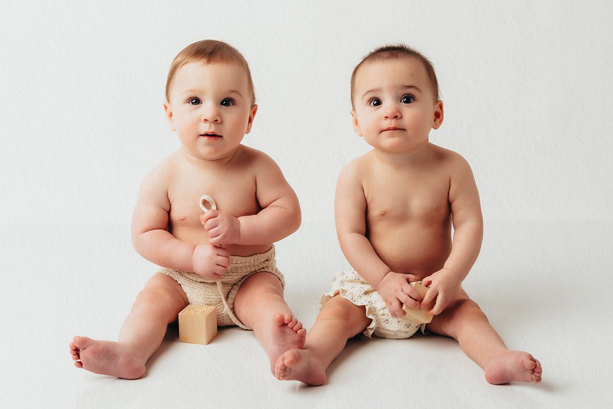 boy girls twins wearing knit diaper covers and sitting against a white backdrop during a Farmington, CT baby photo shoot