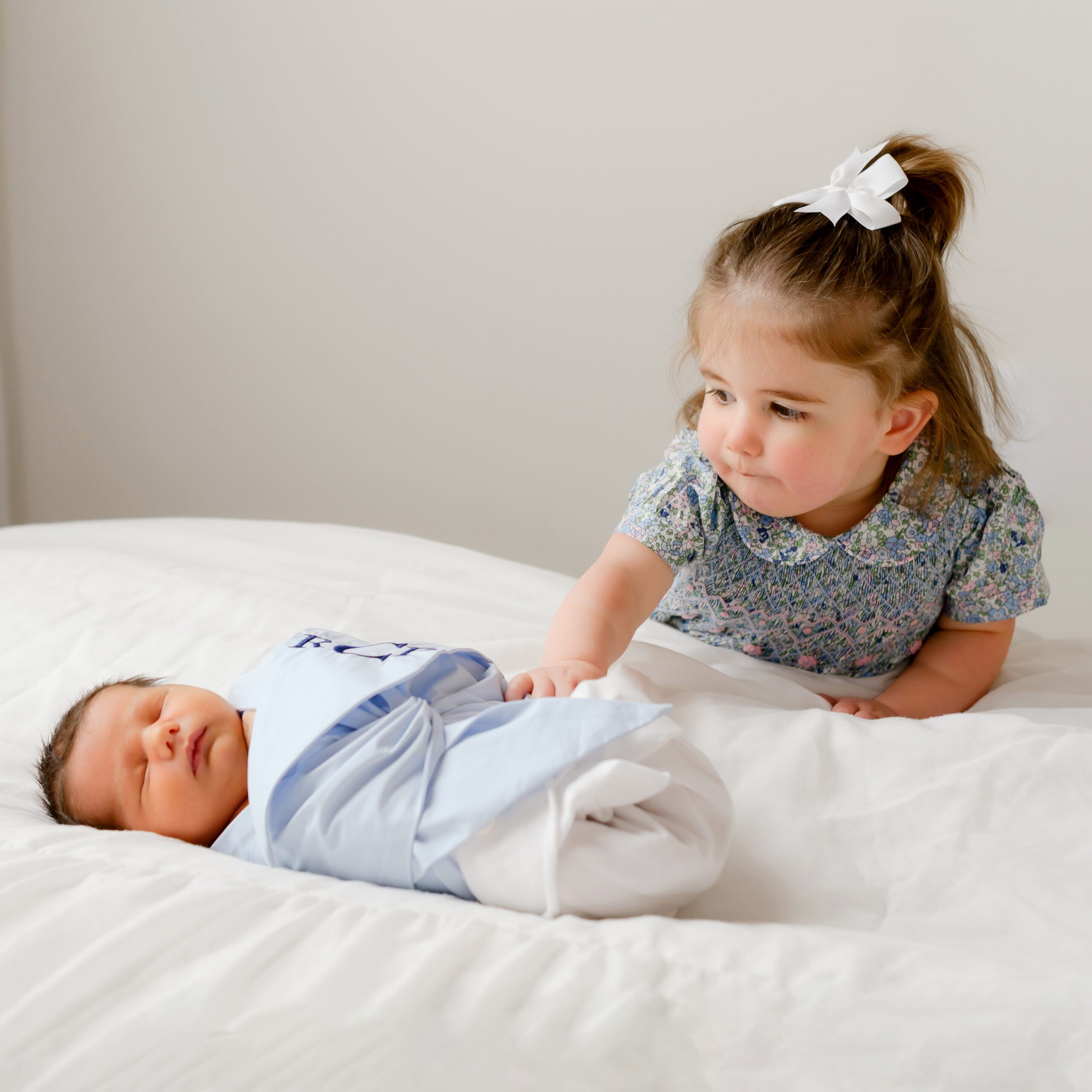 A toddler girl, wearing a floral dress, resting her hand on her newborn baby brother at Kelli Dease Photography in Farmington, CT