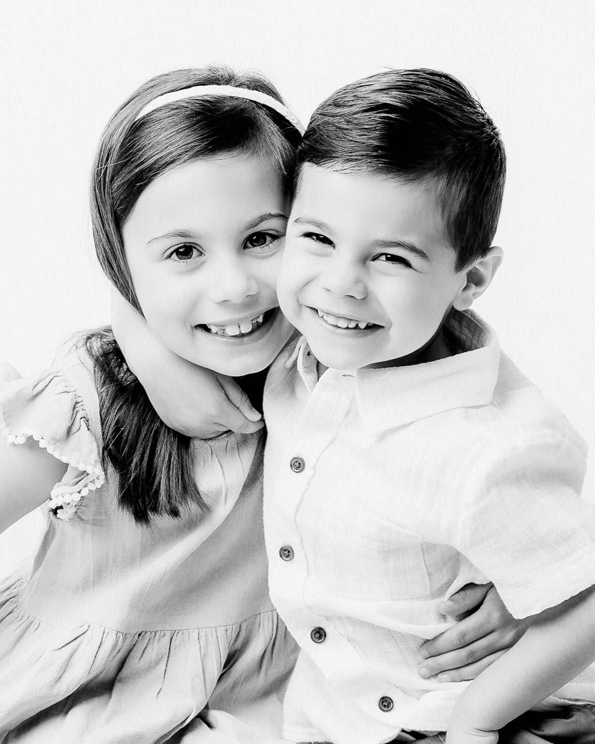 a black and white children's portrait featuring a brother and sister in an embrace.