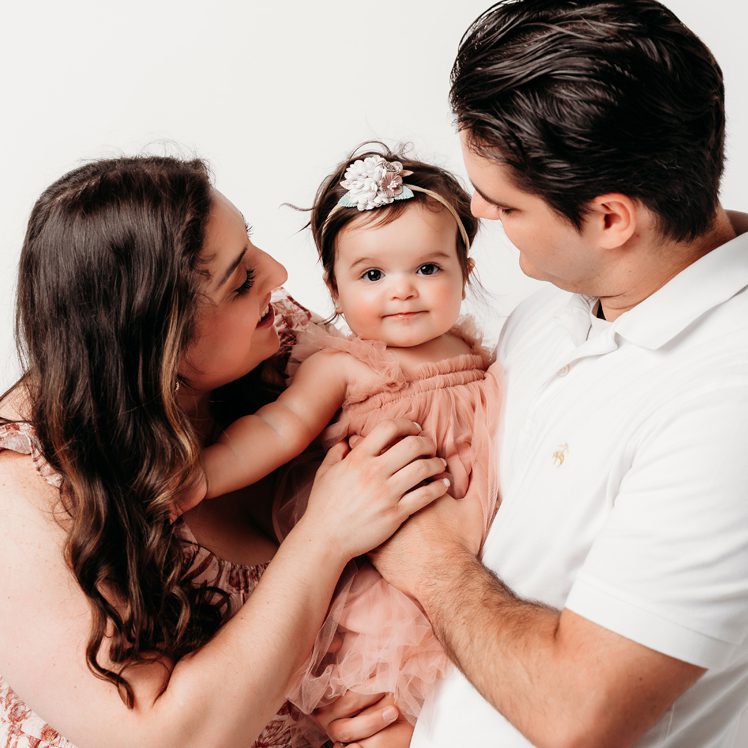 parents leaning in close to their baby girl, laughing together during a first birthday studio session at Kelli Dease Photography