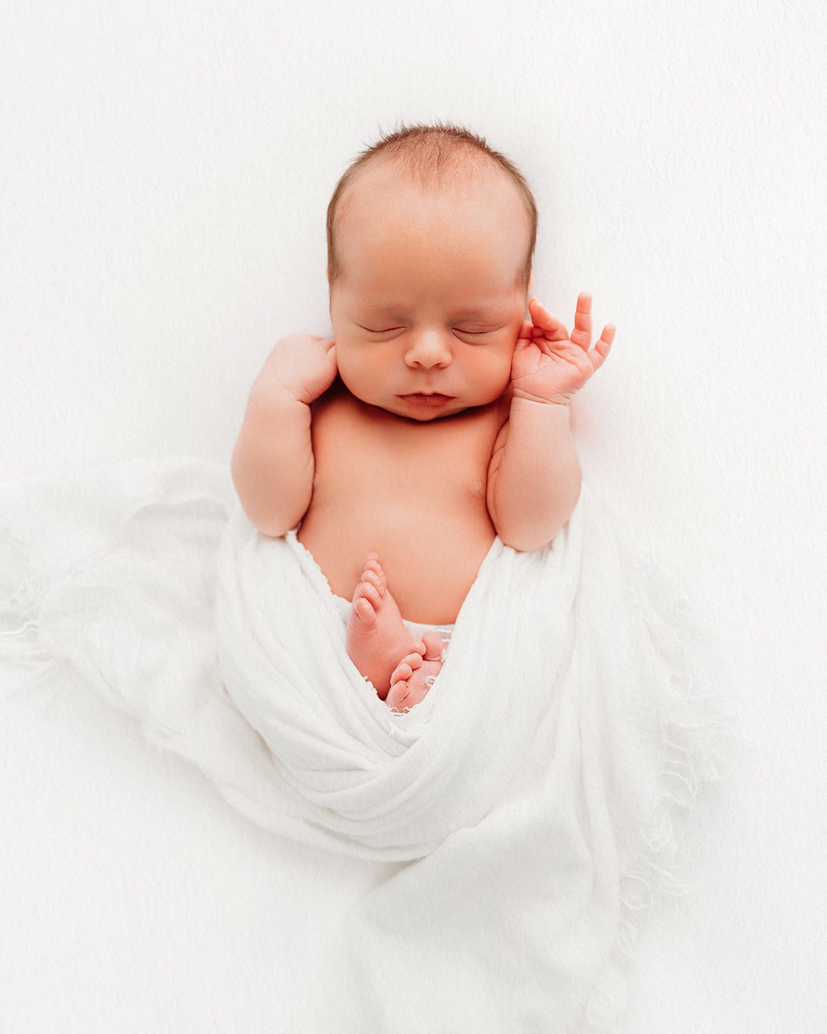 Sleeping newborn baby swaddled in white fabric, hands resting near face - newborn portrait, West Hartford CT