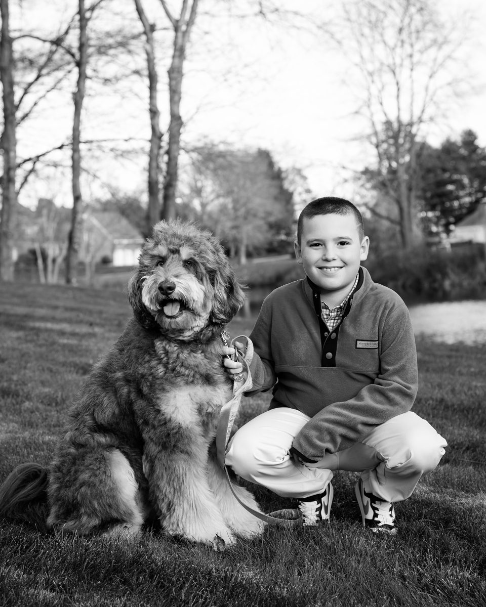 Black and white portrait of a young boy and his dog peeking at their family home in West Hartford, Connecticut by Kelli Dease.