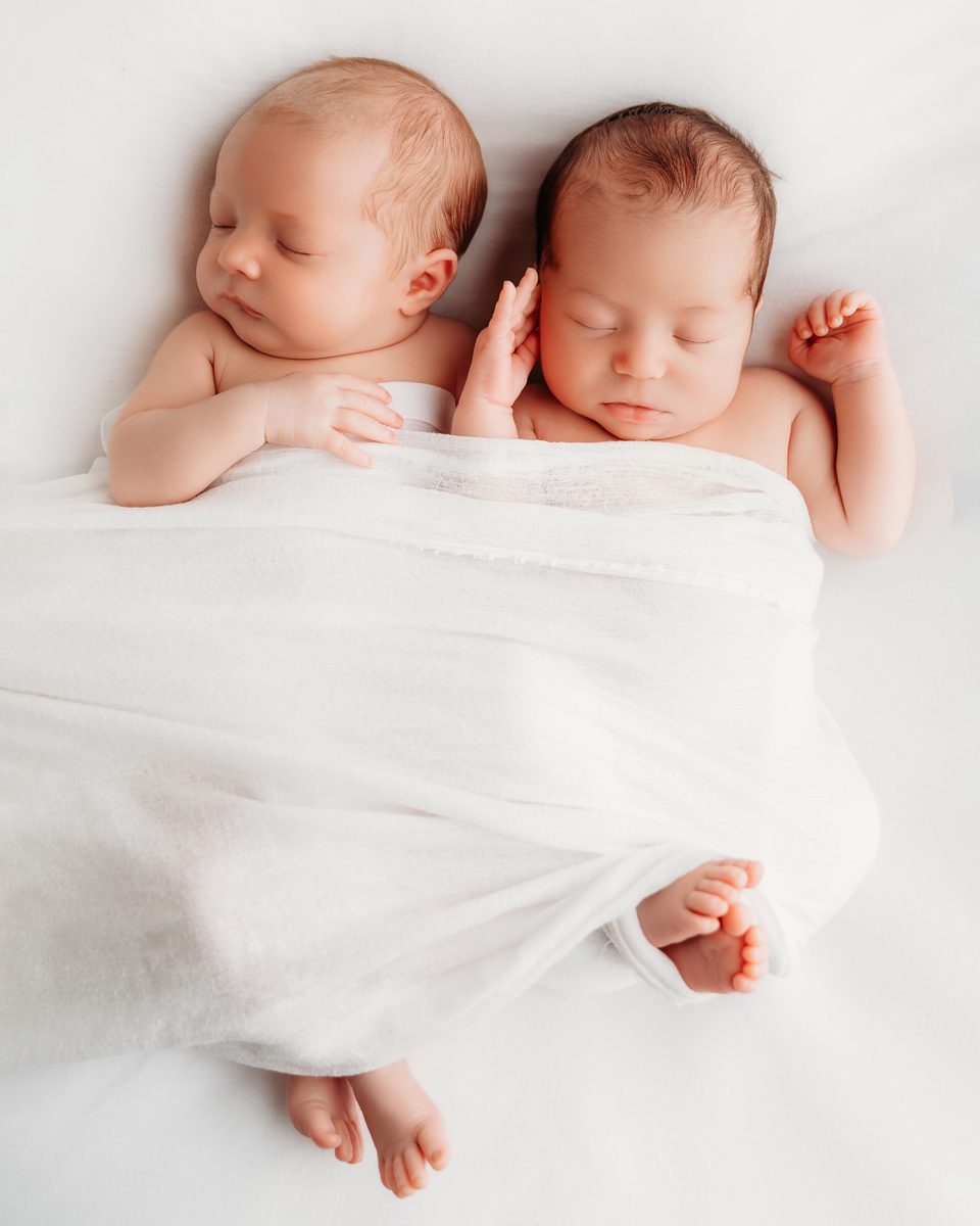 Newborn twins sleeping side by side, swaddled in white, during a studio newborn session near West Hartford CT