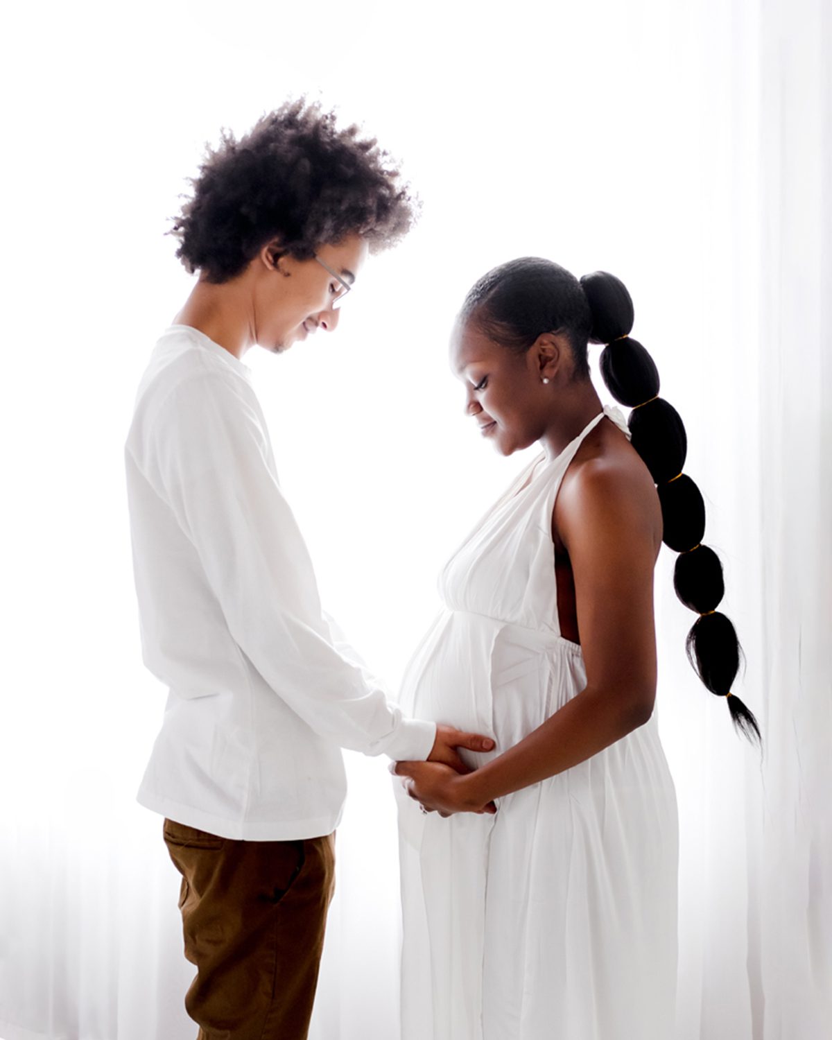 farmington ct studio maternity photography_05 SQ Pregnant woman and her partner facing each other with their hands together on her belly, in a bright white studio at Kelli Dease Photography, Farmington CT
