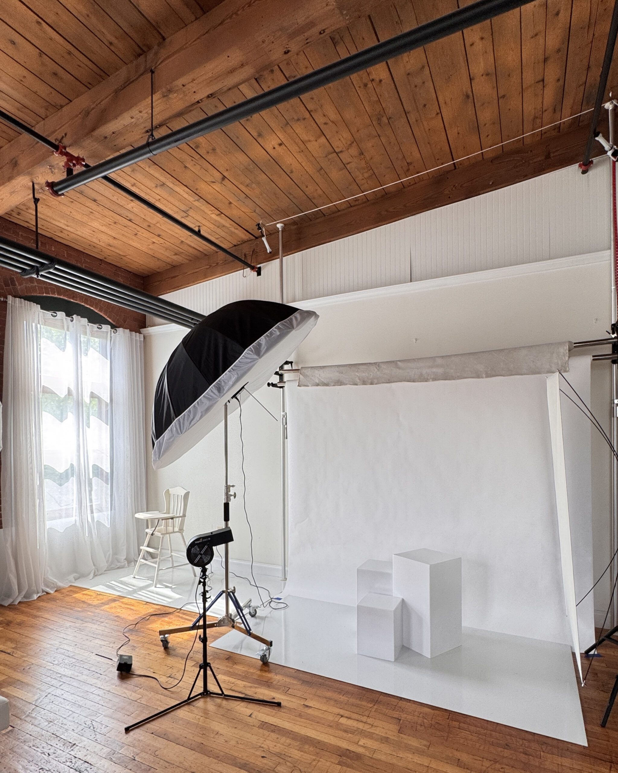 Bright newborn and family photography studio at Kelli Dease Photography in Farmington, CT, with a white backdrop, softbox lighting, and tall curtained windows.